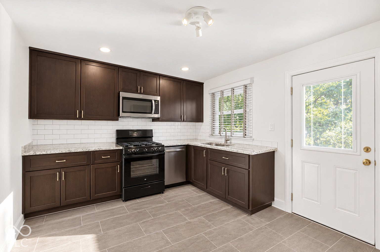 Kitchen featuring dark wood cabinetry, light-toned countertops, subway tile backsplash, and stainless steel appliances