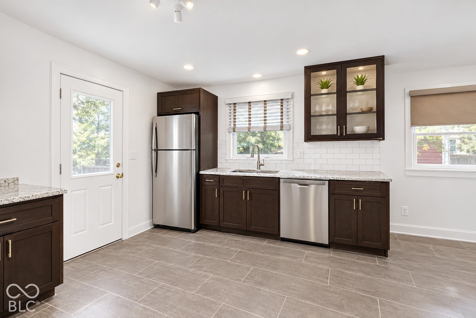 Dark wood-finish cabinetry, light stone countertops, stainless steel appliances, subway tile backsplash, and recessed lighting
