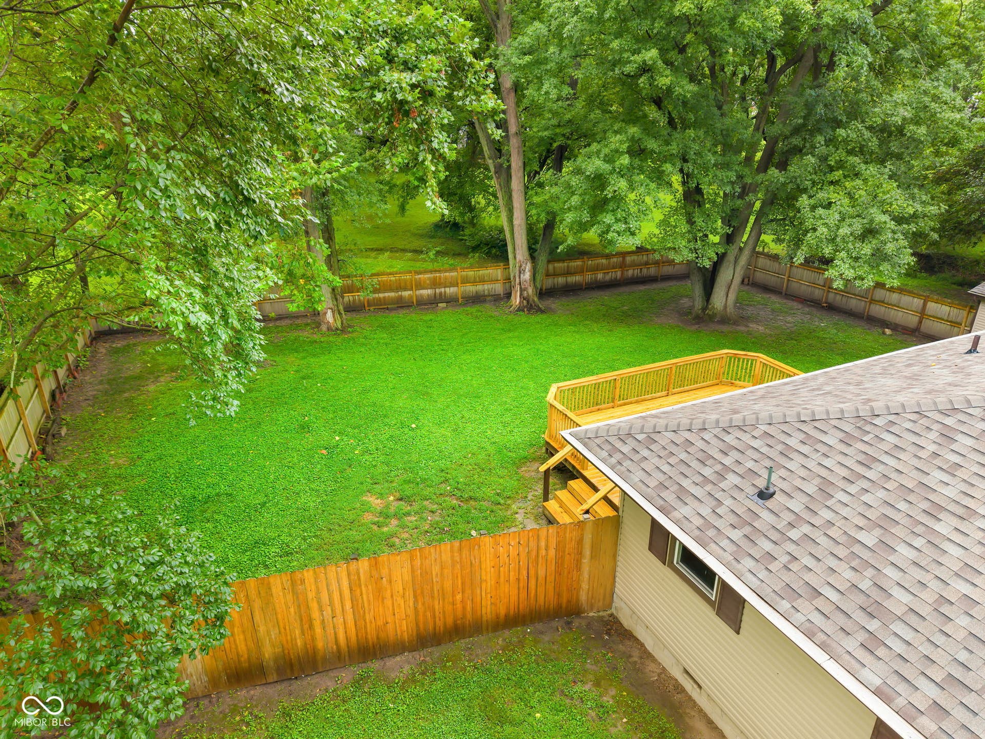 Expansive green lawn with a wood privacy fence, large mature trees, and a spacious wood deck