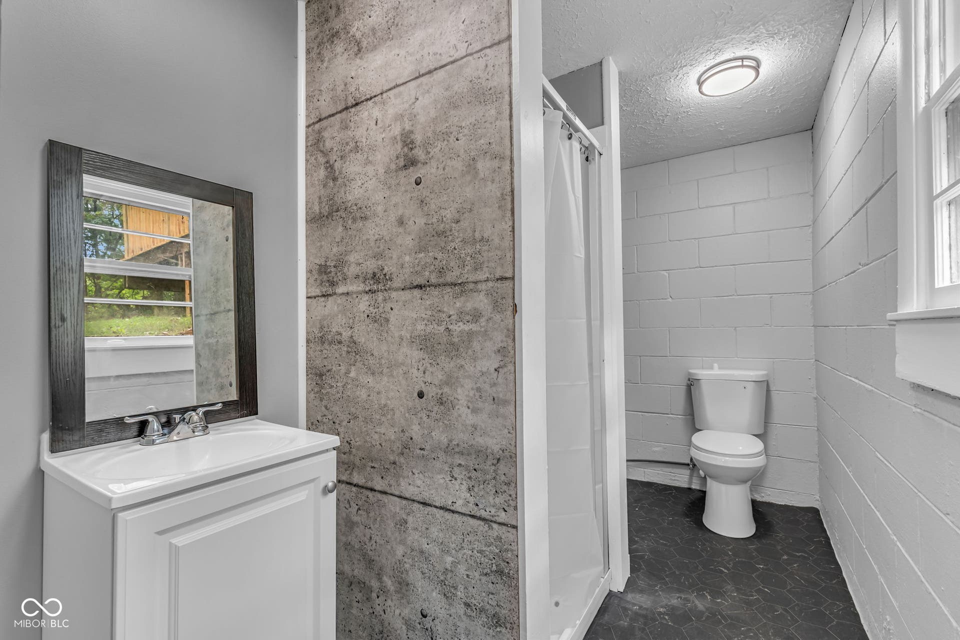 White vanity with integrated sink, framed mirror, and modern concrete-finish accent wall