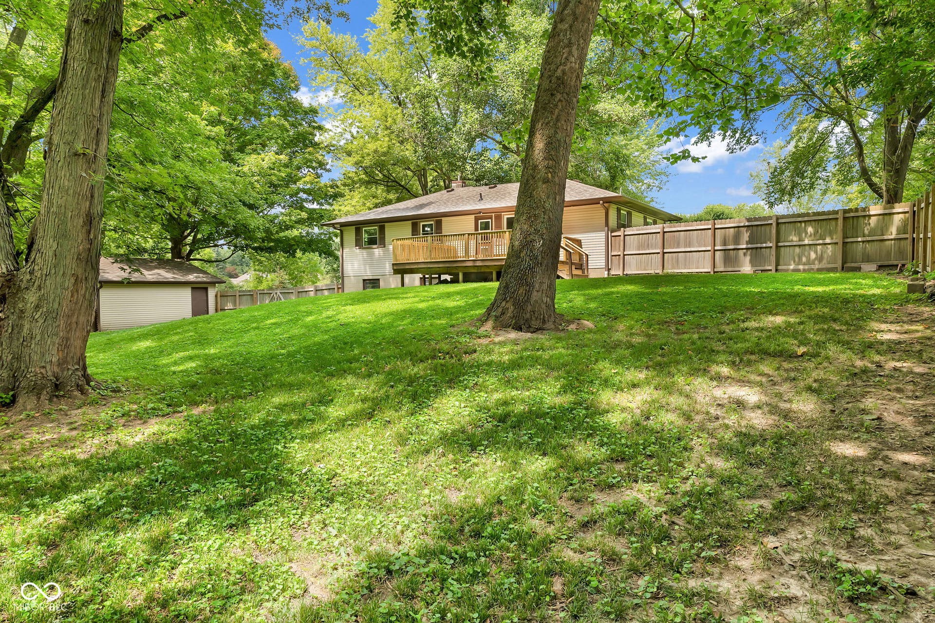 Sloped backyard featuring established trees, a wooden privacy fence, and a detached shed
