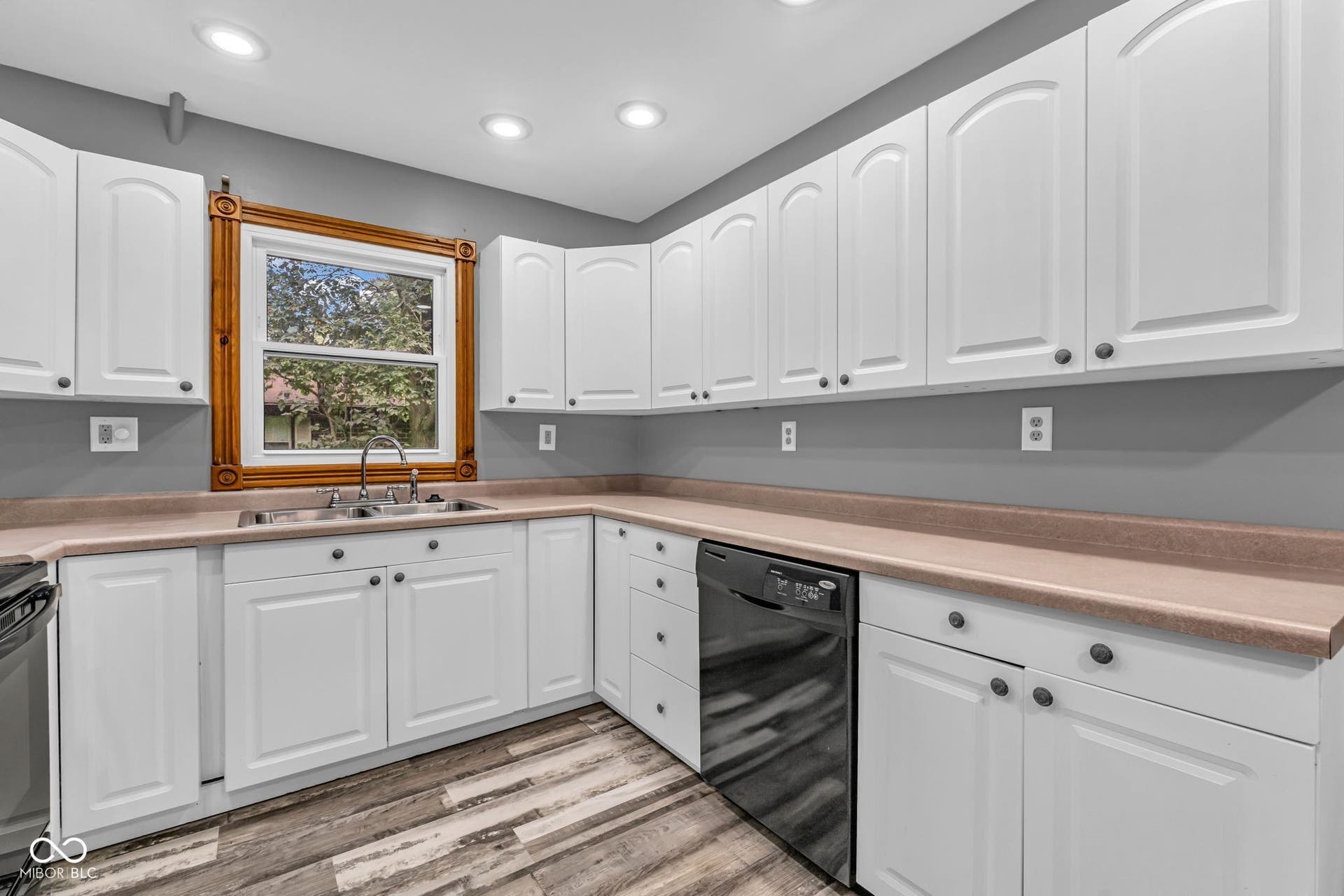 White cabinetry, neutral countertops, wood-finish flooring, stainless steel sink, and a black dishwasher