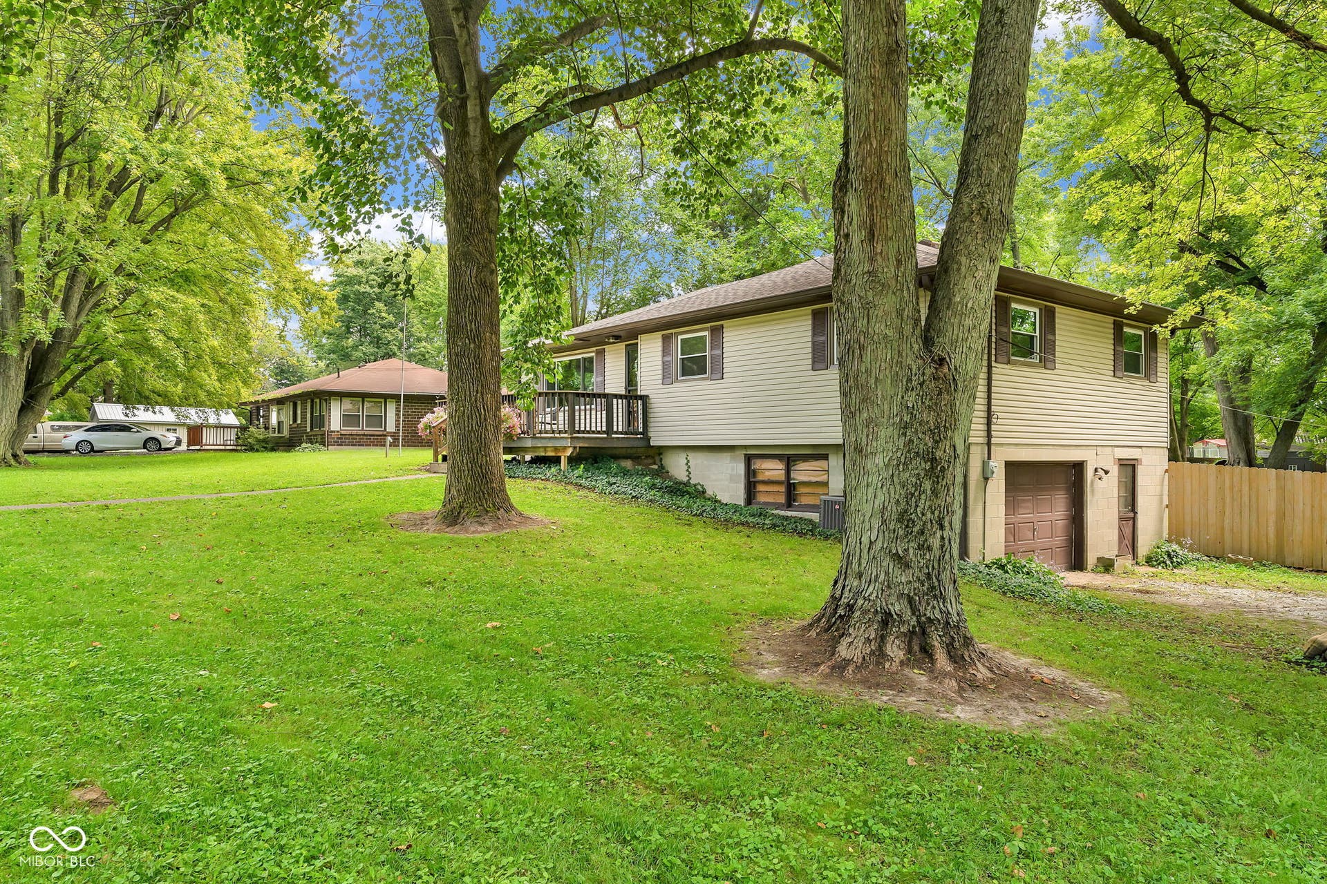 Split-level residence featuring beige siding, brown window shutters, and a brown garage door