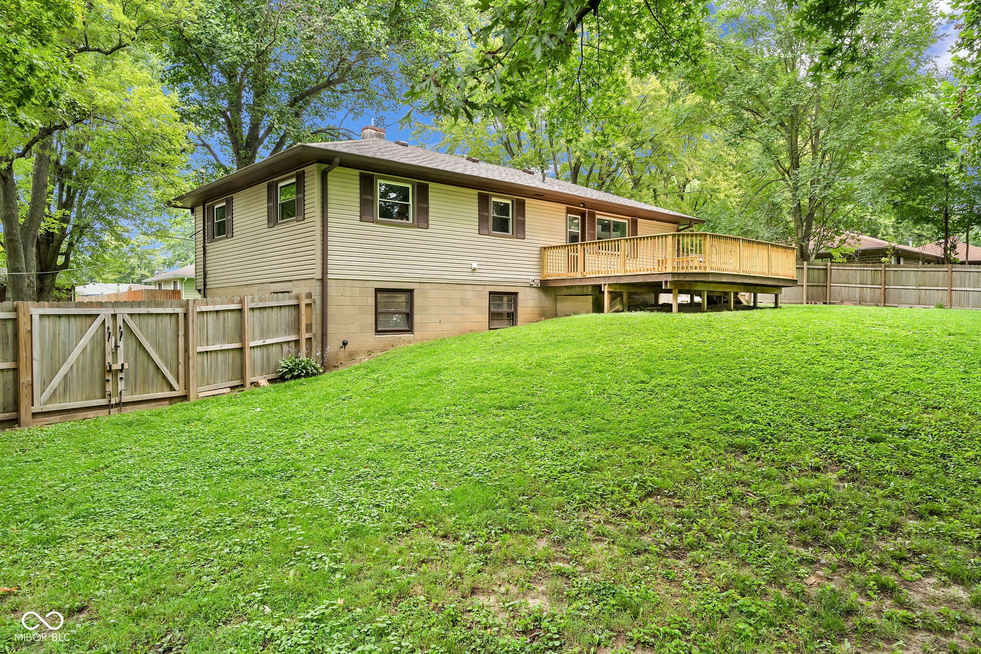 Expansive backyard featuring a manicured lawn, a wooden privacy fence, and a large elevated wood deck