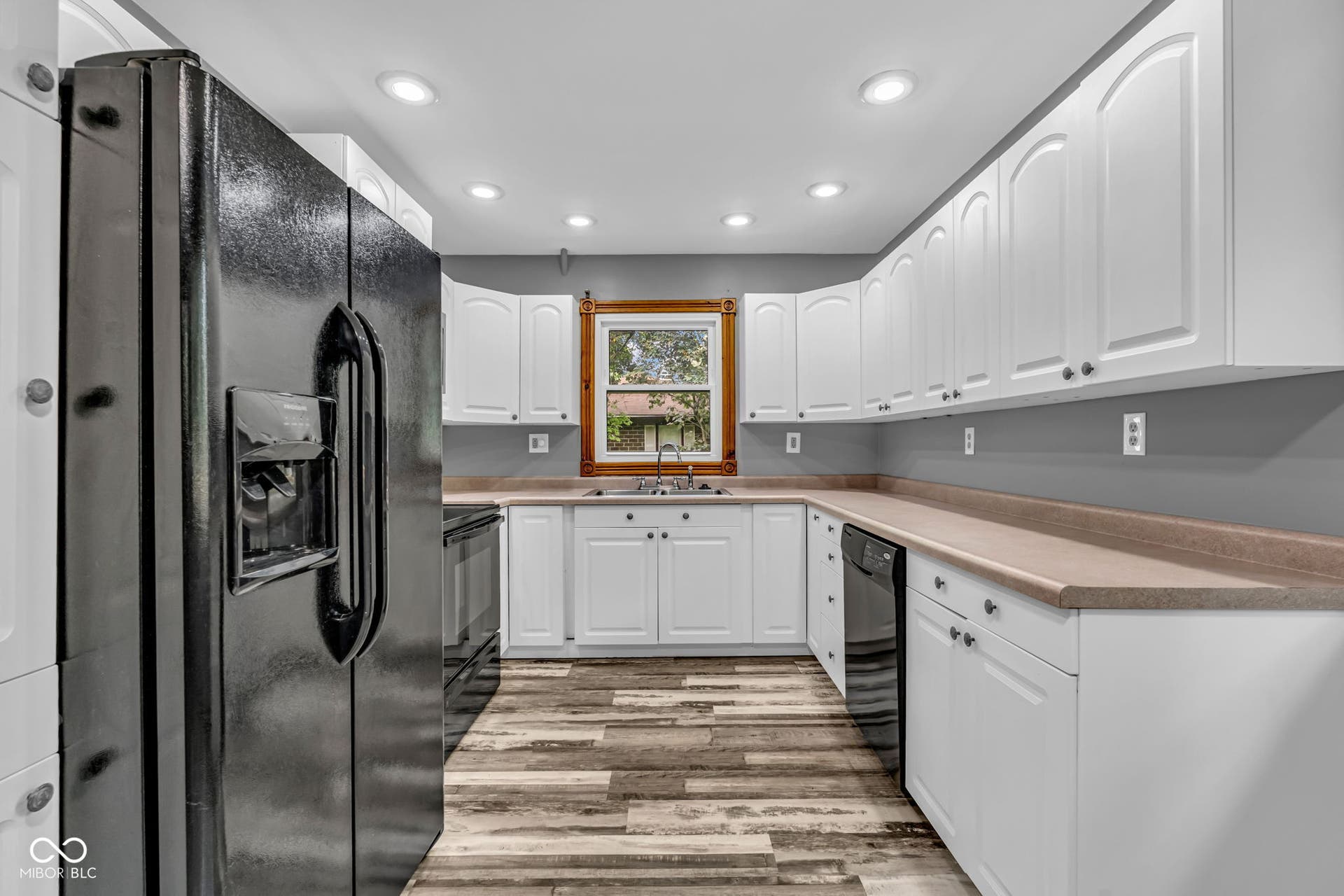 Kitchen with white cabinetry, black appliances, recessed lighting, wood-finish flooring, and a window with wood trim