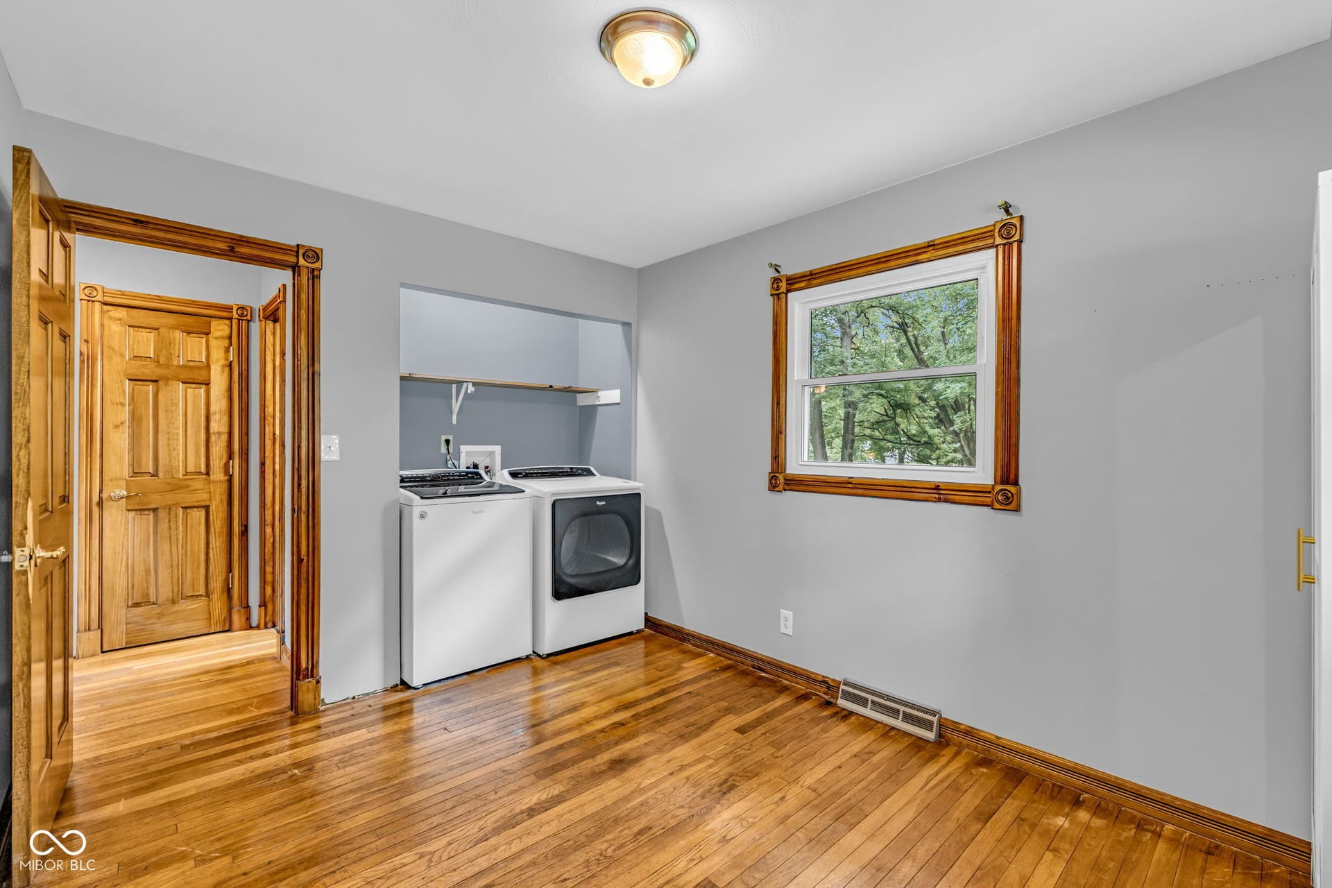 Hardwood flooring throughout, recessed laundry area with shelving, and a window with wood trim