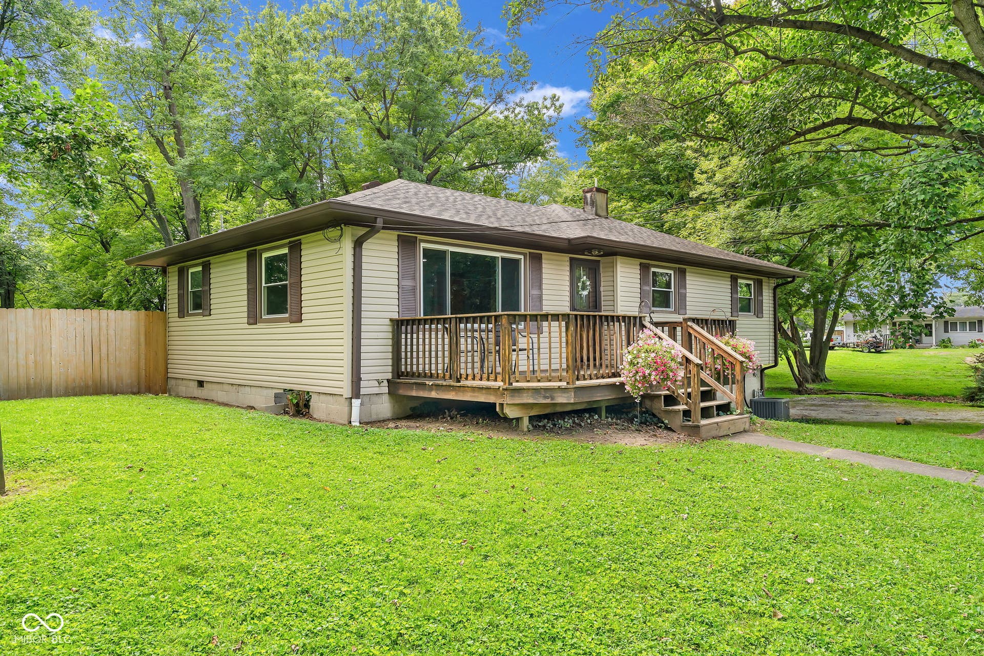 Exterior featuring light-colored siding, a dark-toned roof, a wooden front deck with railings, and a privacy fence