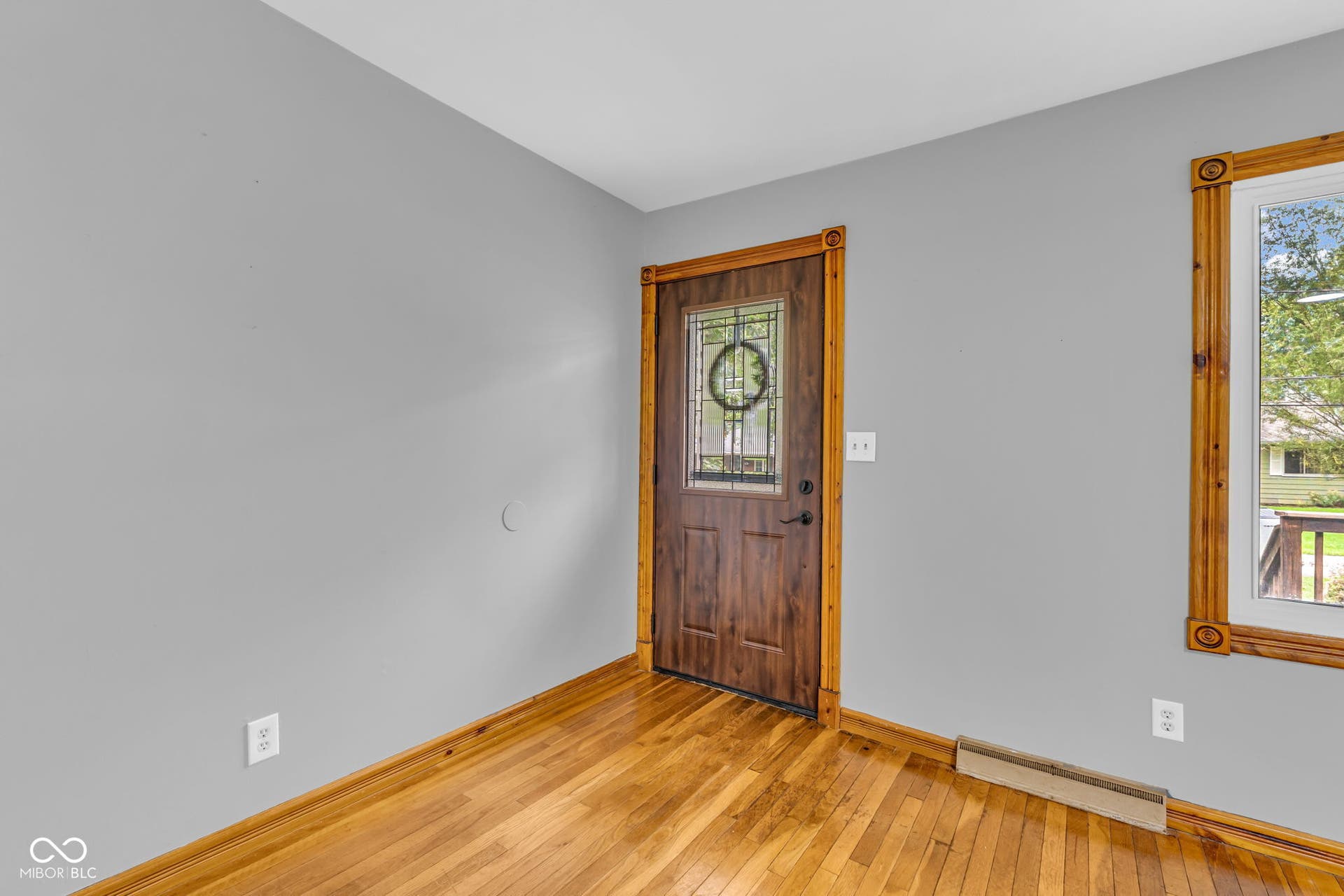 Wood-finish flooring, light gray wall paint, and a wood-paneled door with decorative glass inlay