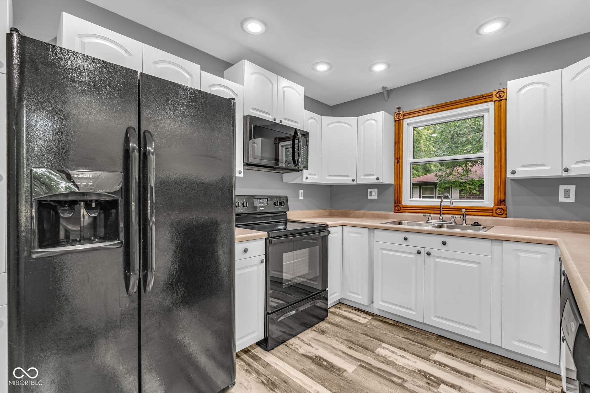 White cabinetry, black appliances, light-toned countertops, wood-finish flooring, and recessed lighting