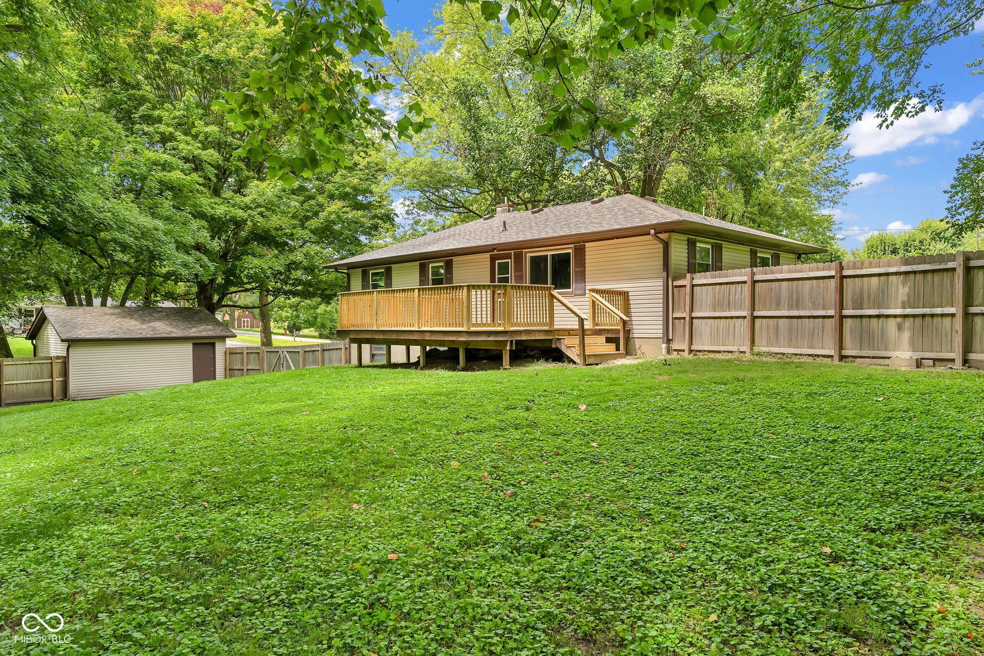 Expansive backyard with a wooden deck, privacy fencing, and a detached storage shed
