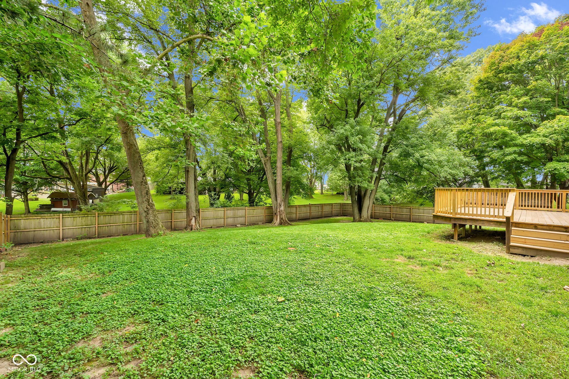 Expansive green lawn with mature trees, surrounded by a wooden privacy fence, featuring a multi-level wood deck