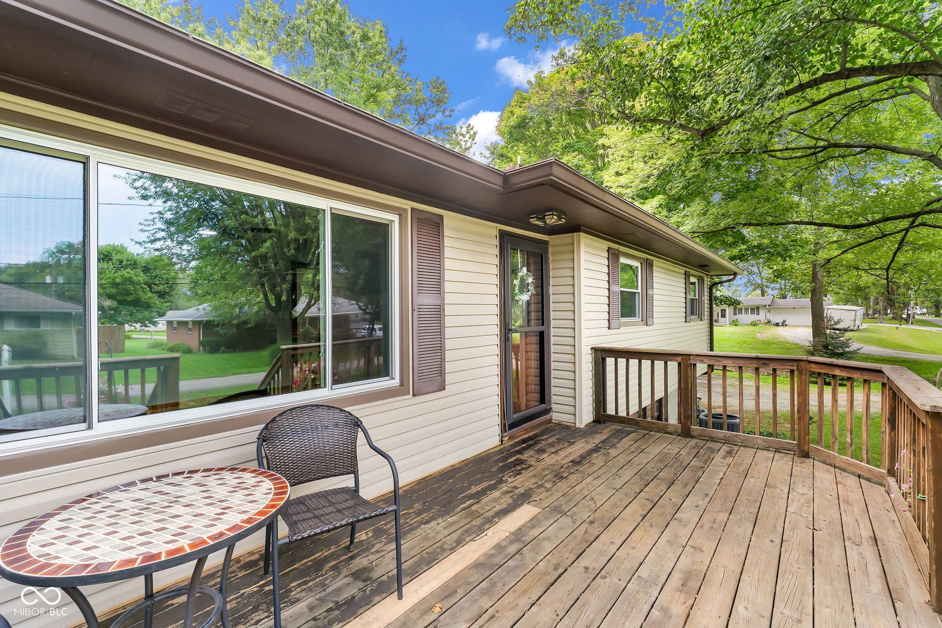 Expansive wood deck with railing, featuring a large sliding window, a side entrance, and light-toned siding