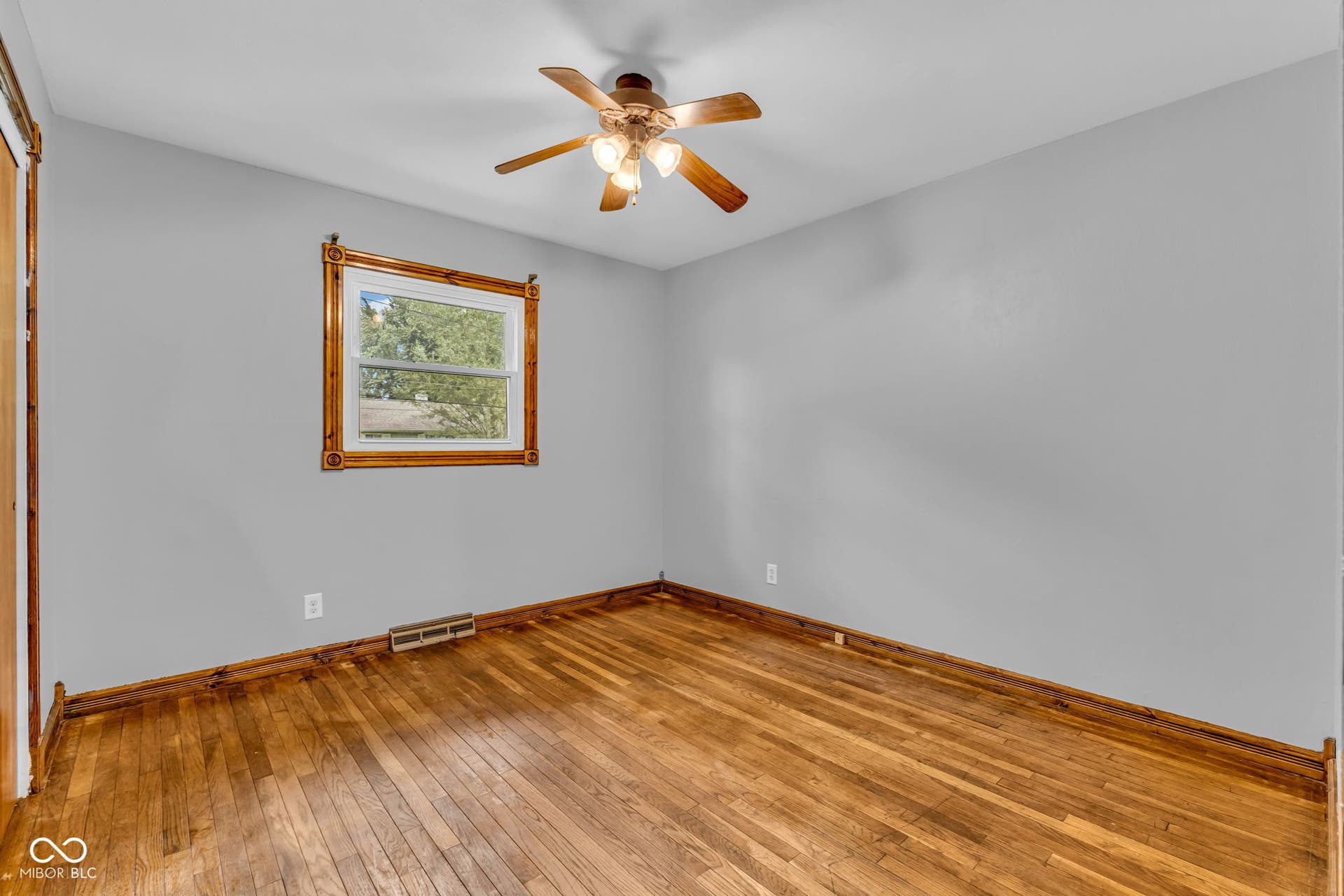 Wood-finish flooring, light gray wall paint, wood window trim, wood-finish ceiling fan with integrated lighting, and wood-finish door frame