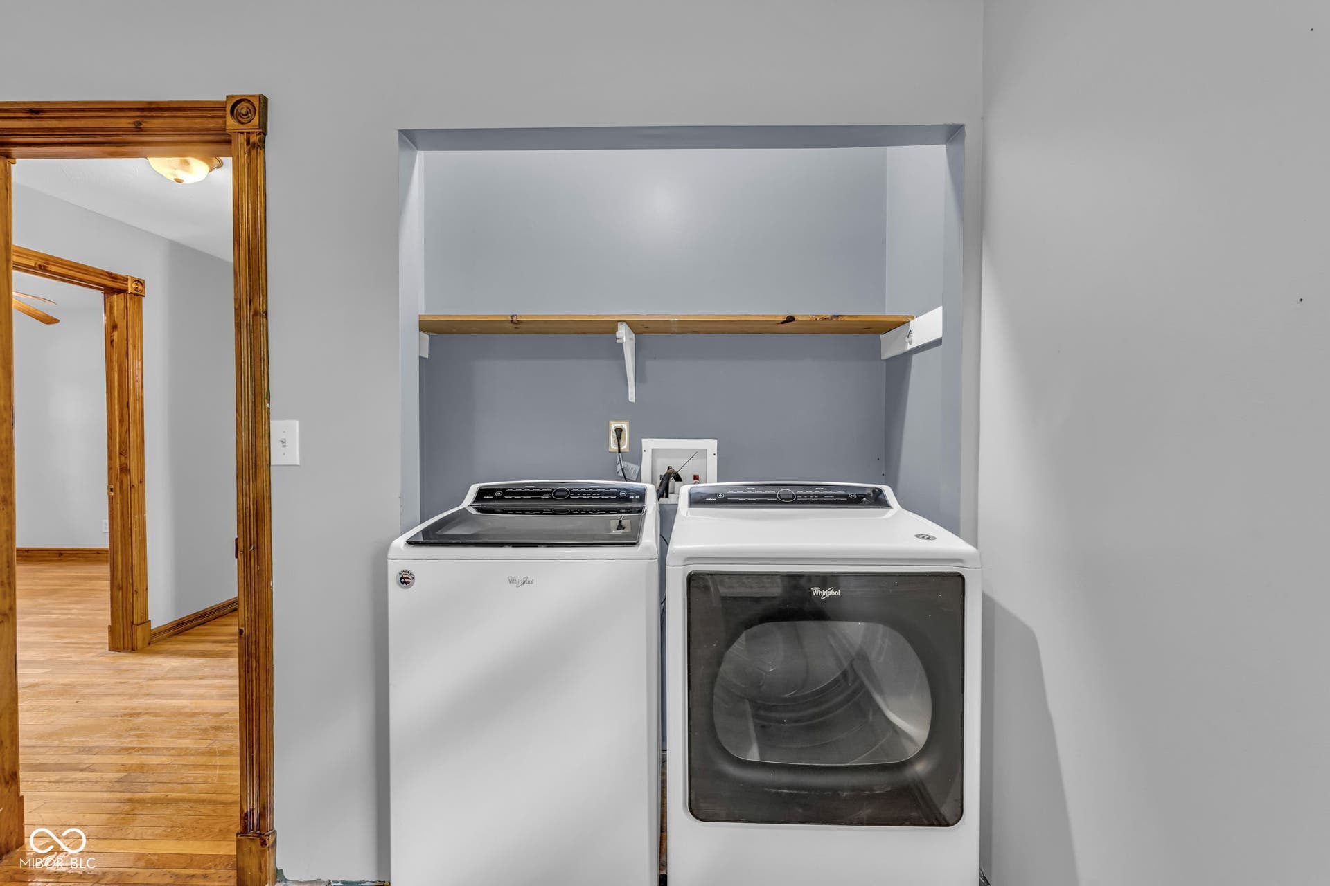 Dedicated laundry area with a built-in wood-finish shelf and wood-finish flooring