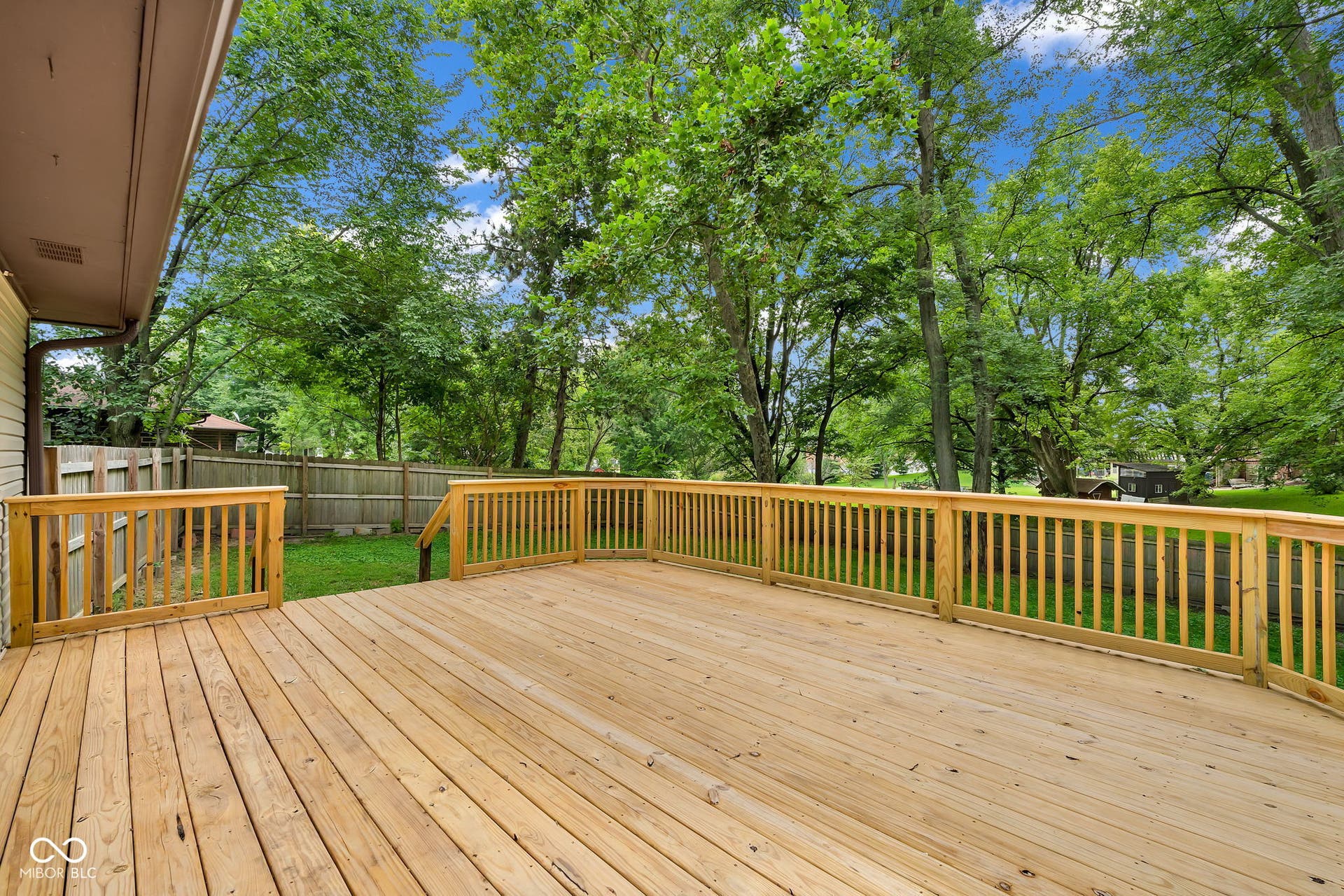 Expansive wood deck with natural wood railing, surrounded by mature trees and a fenced yard