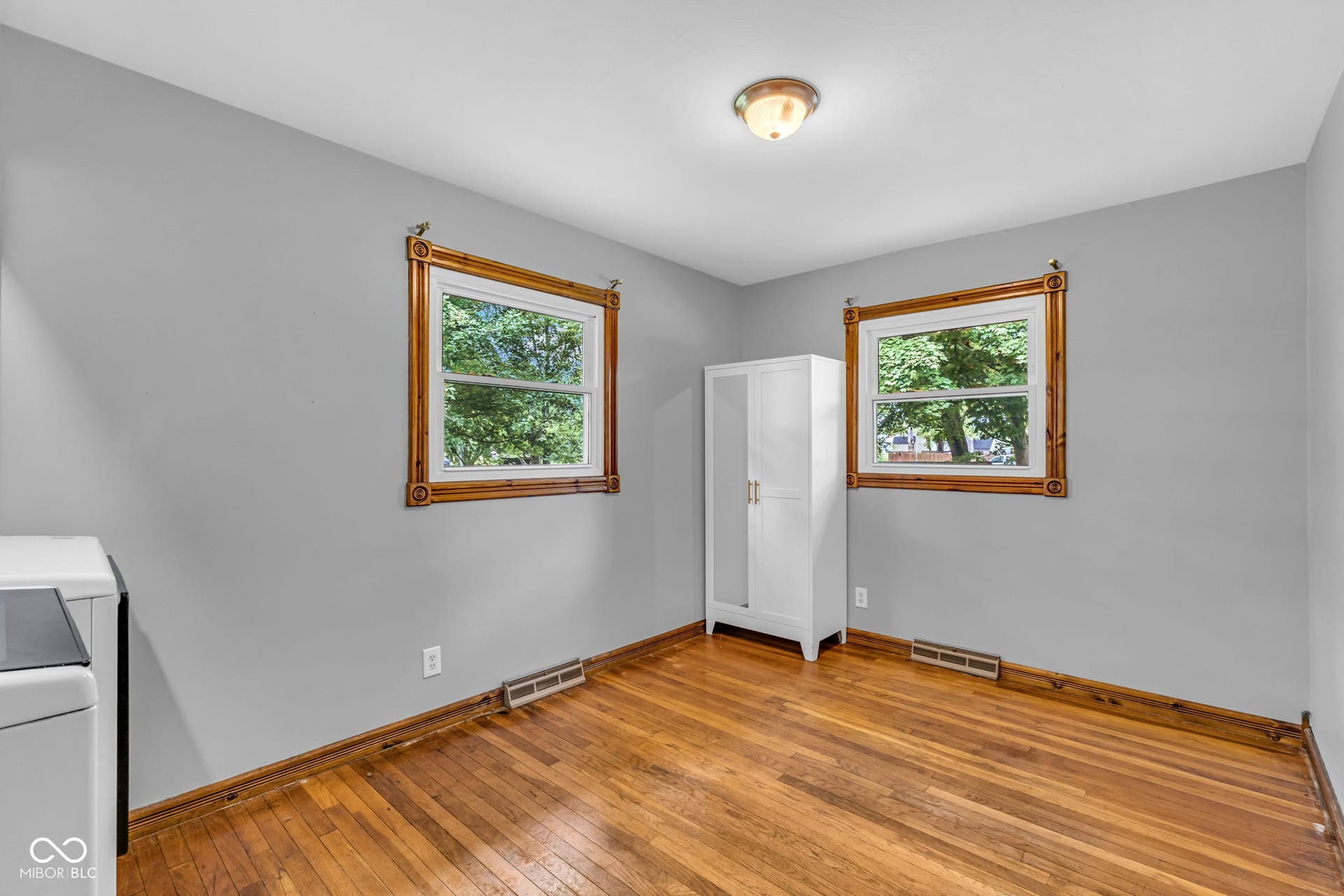 Hardwood flooring, two windows with wood trim, and a flush-mount ceiling light fixture