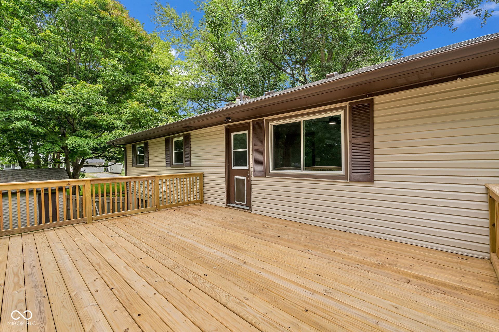Expansive wood deck with wood railing, tan horizontal siding, and brown exterior trim
