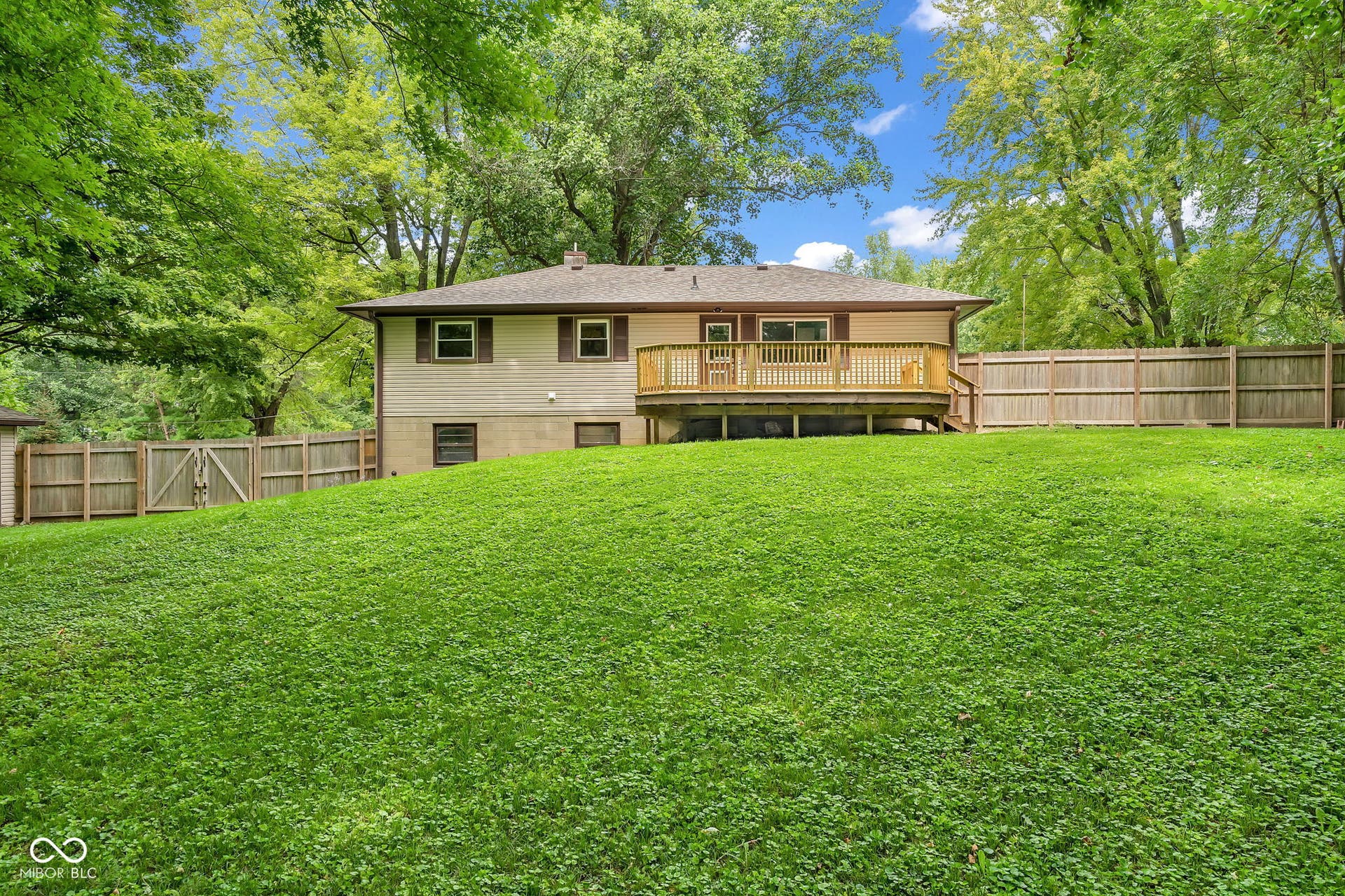 Expansive backyard with a wooden fence, mature trees, and a raised wood deck