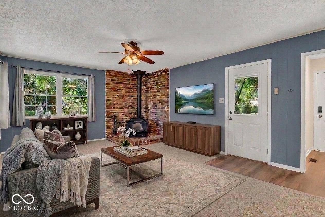 Brick-clad wood-burning stove with hearth, wood-finish flooring, and a ceiling fan with integrated lighting