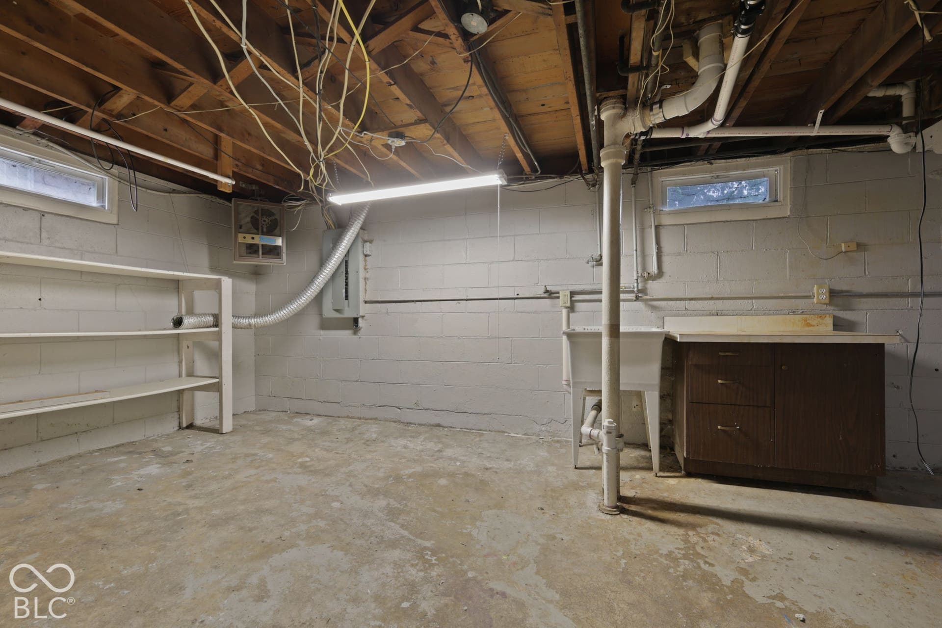 Unfinished space featuring painted concrete block walls, concrete flooring, built-in wooden shelving, a utility sink, and wood-finish storage cabinetry