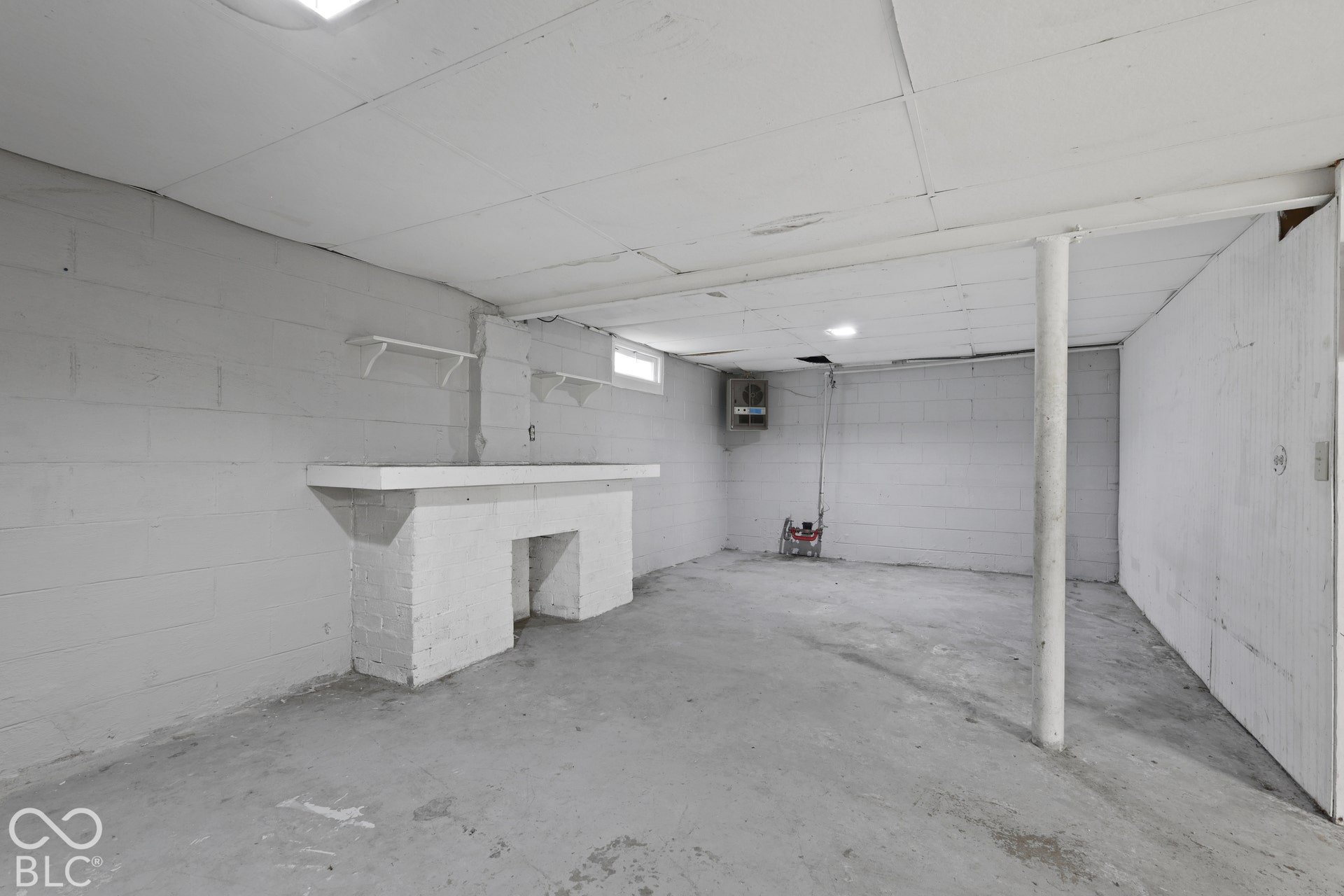 Painted concrete block walls, ceiling tile system, concrete flooring, built-in masonry mantel, and vertical structural support column