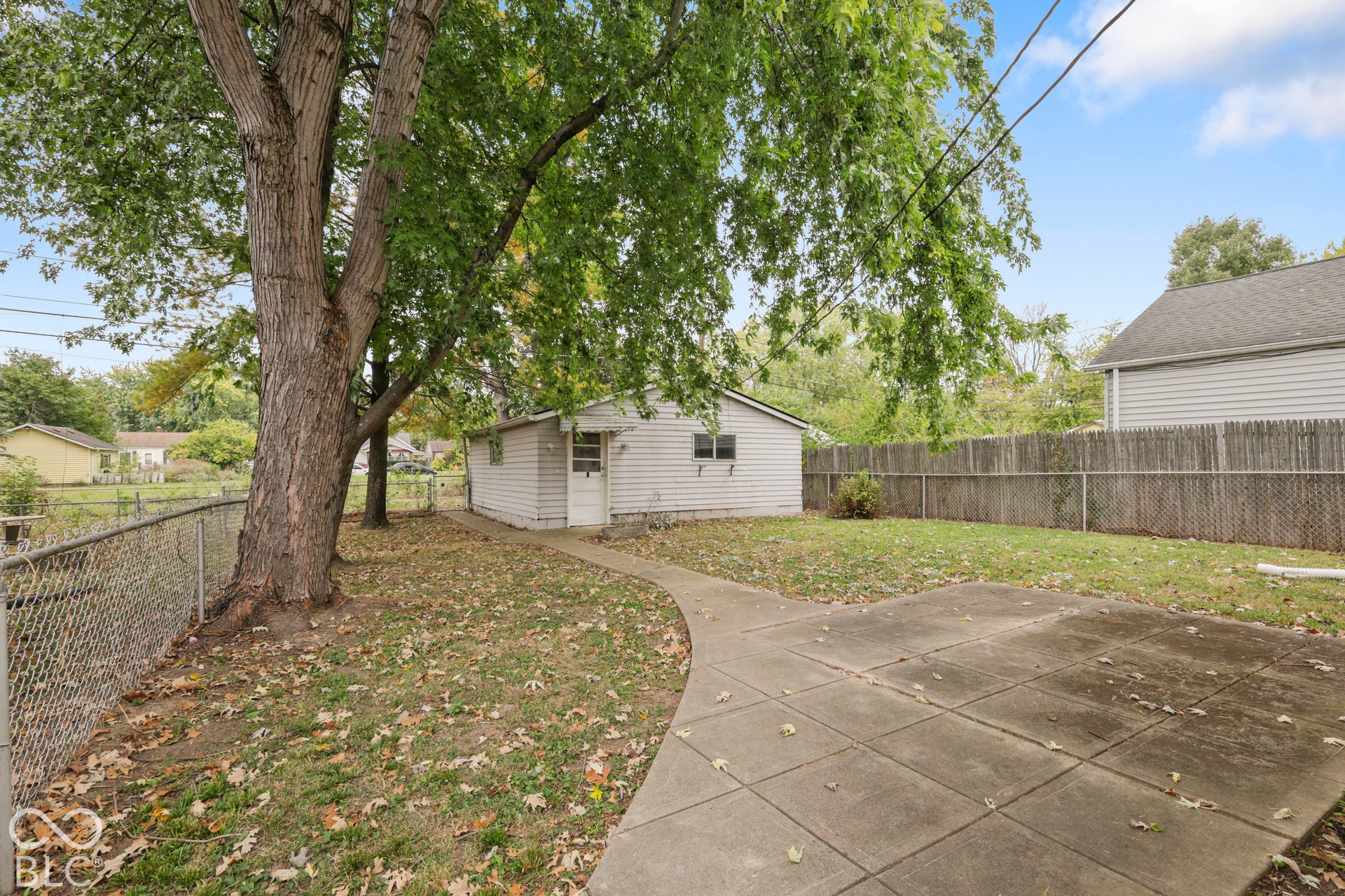 Rear yard featuring a detached structure, concrete patio, mature tree, and perimeter fencing