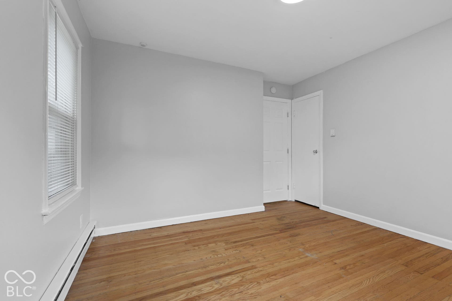 Room featuring wood-finish flooring, neutral walls, a single-hung window with blinds, and two solid-core paneled doors