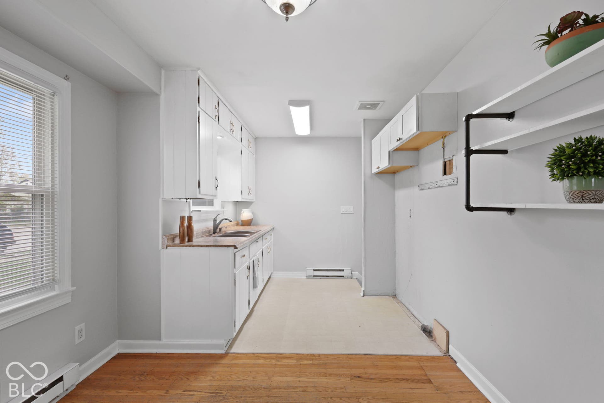 Kitchen featuring white cabinetry, wood-finish flooring, a stainless steel sink with a faucet, and industrial-style wall-mounted shelving
