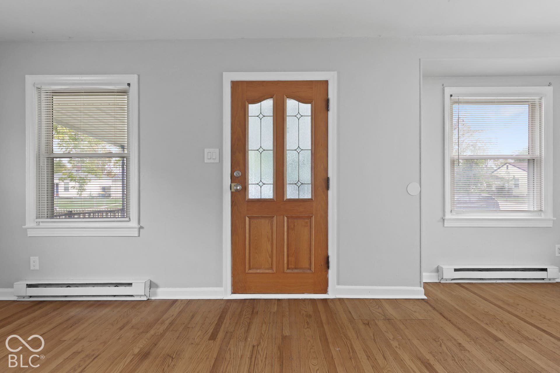 Wood-finish flooring, light grey walls, and a wood-tone entry door featuring two decorative glass panels and dual-pane windows with white trim