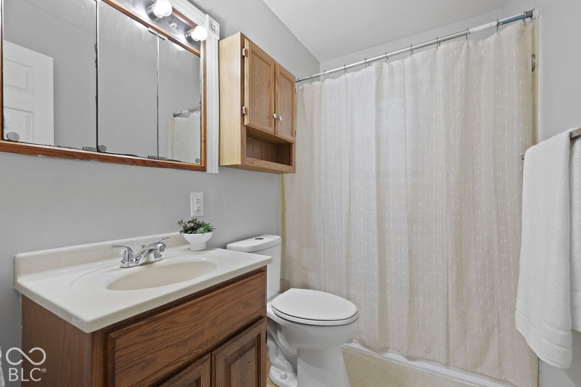 Bathroom featuring a wood-finish vanity with an integrated basin, mirrored medicine cabinet, wall-mounted wood cabinet, and a shower-tub combination
