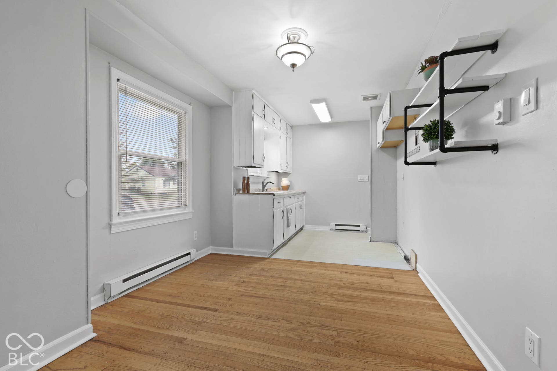 Kitchen area featuring wood-finish flooring, white cabinetry, integrated sink, overhead lighting fixtures, and industrial-style wall-mounted shelving