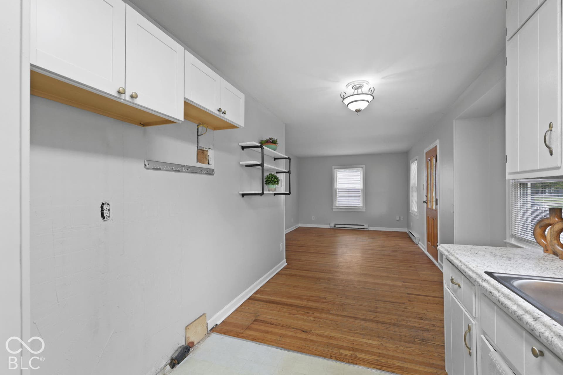 Kitchen area featuring white shaker-style cabinetry, stone-finish countertops, wood-finish flooring, and built-in wall shelving