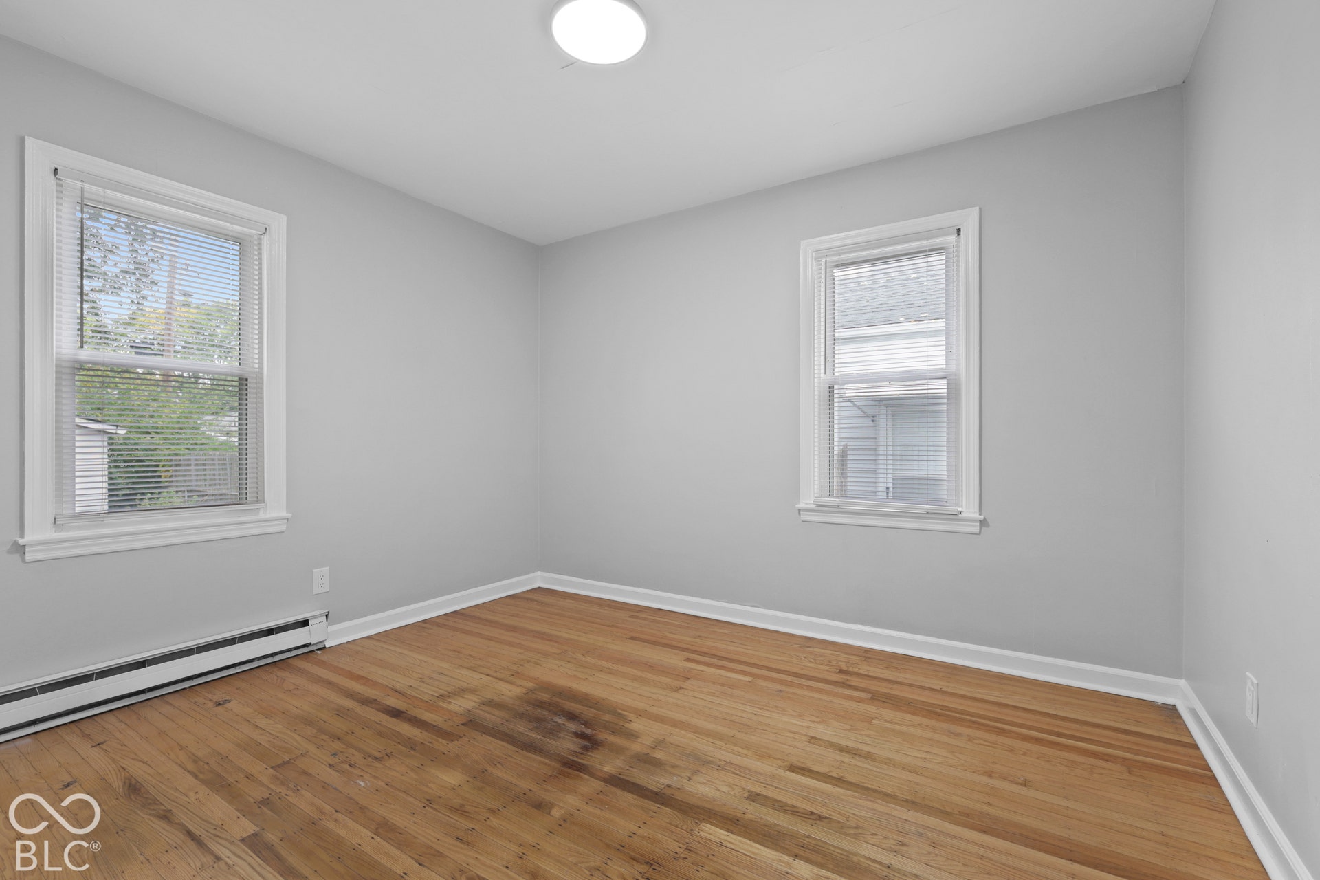Neutral-toned walls featuring wood-finish flooring, two double-hung windows with white casings, and a flush-mount ceiling light fixture