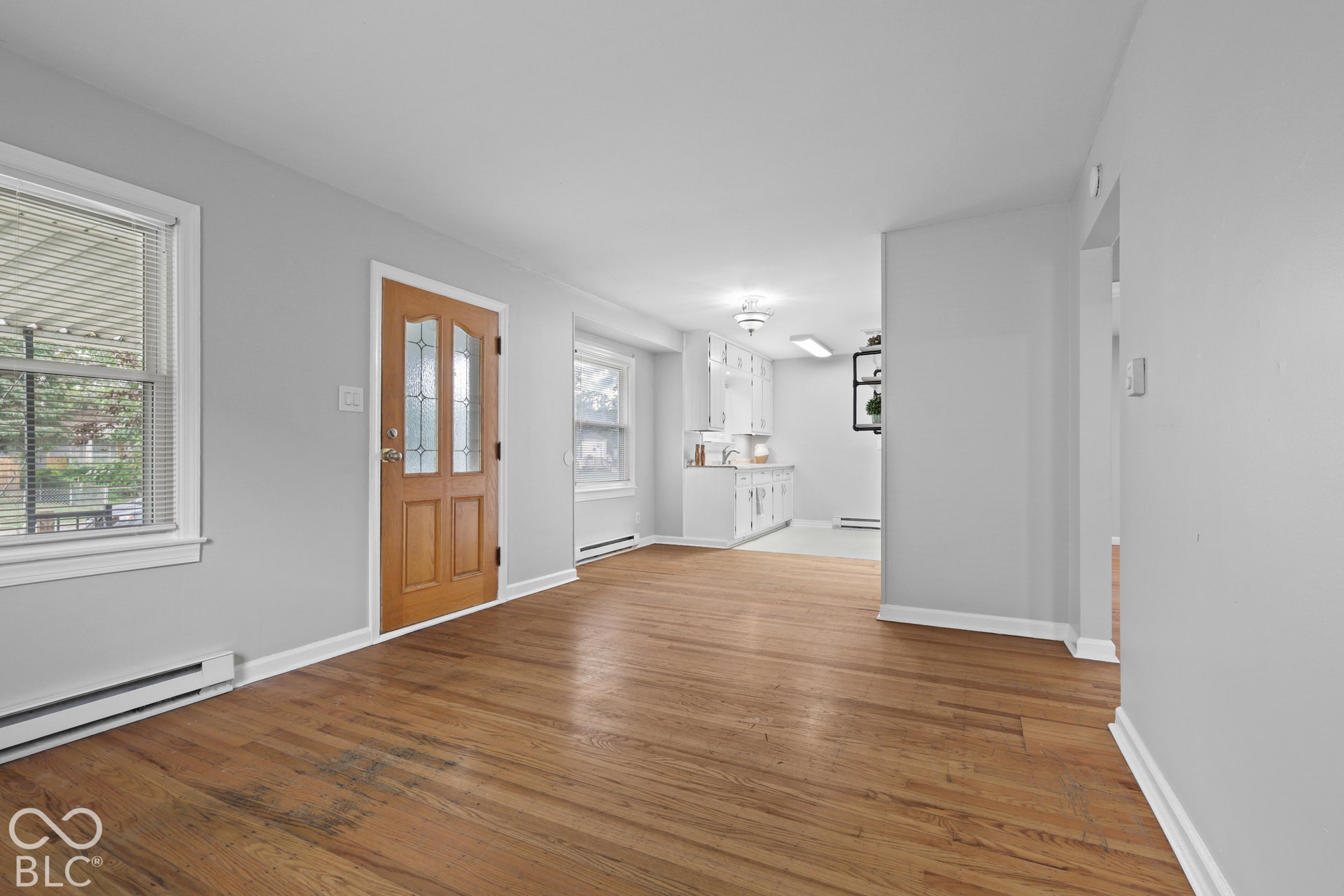 Interior space featuring hardwood flooring, a natural wood-finish door with decorative glass inlay, and white cabinetry in the kitchen area