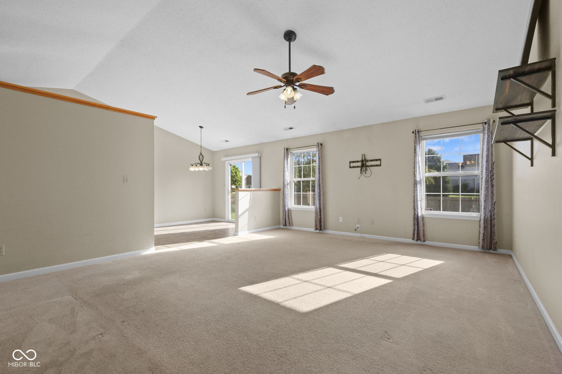 Spacious living room featuring vaulted ceilings, carpet, abundant natural light, and an open connection to the dining area.