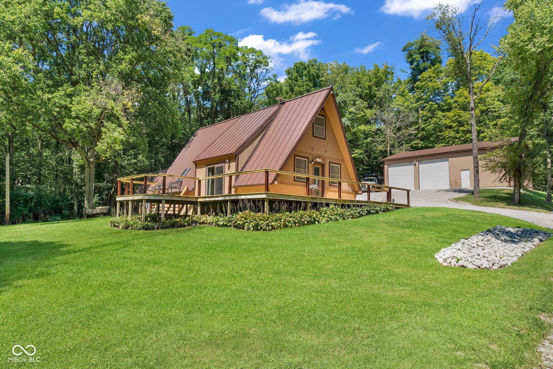 5432 W Whittier Drive, Knightstown, IN 46148 A-frame residence featuring a metal roof, expansive wraparound deck, and lush surrounding trees