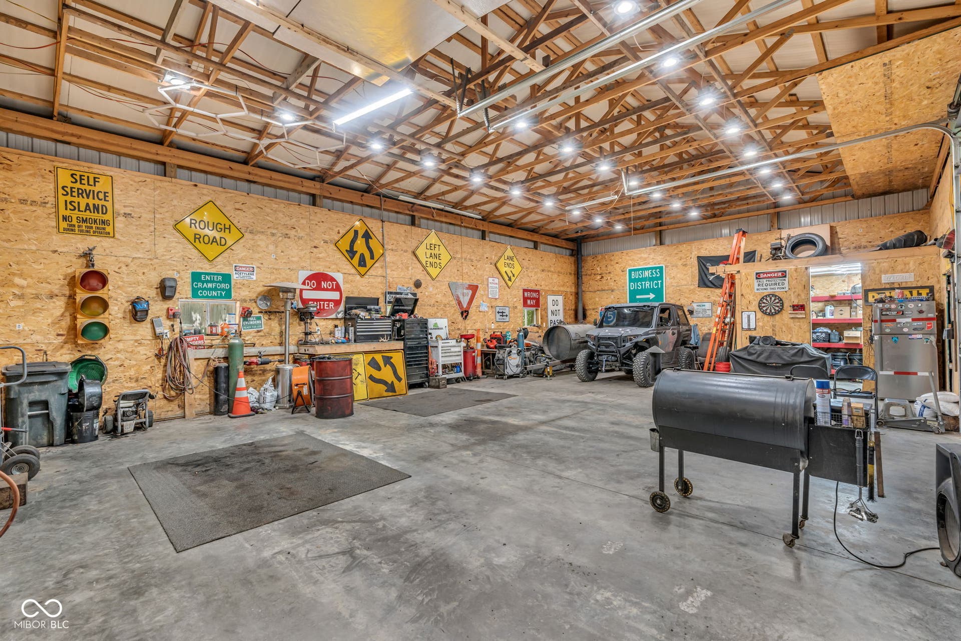 5432 W Whittier Drive, Knightstown, IN 46148 Expansive garage space featuring a concrete floor, exposed wood beam ceiling, and ample overhead lighting
