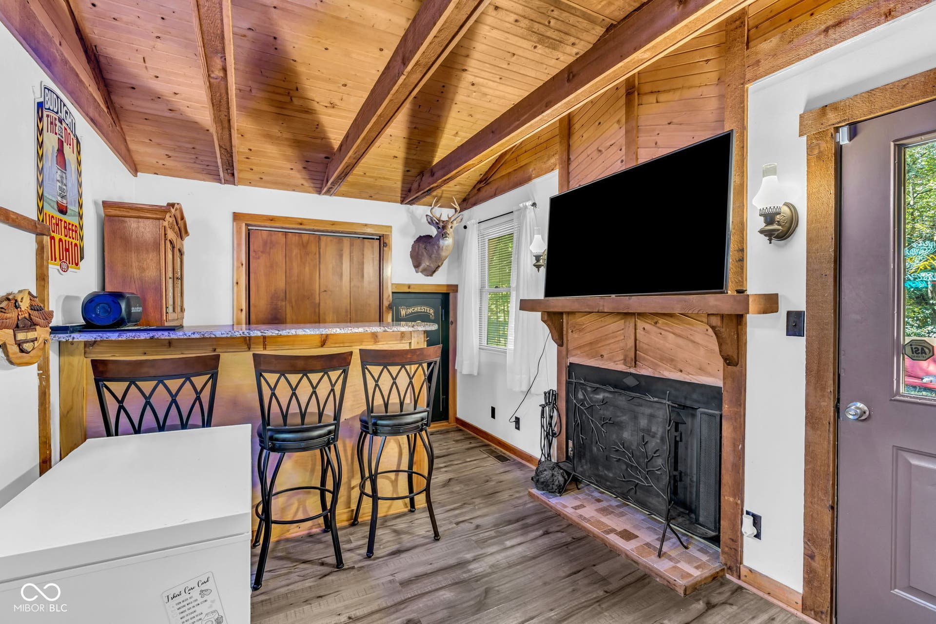 5432 W Whittier Drive, Knightstown, IN 46148 Wood-finish flooring, wood plank ceiling with exposed beams, stone-look bar countertop, wood-paneled fireplace with mantel, and built-in wood cabinetry