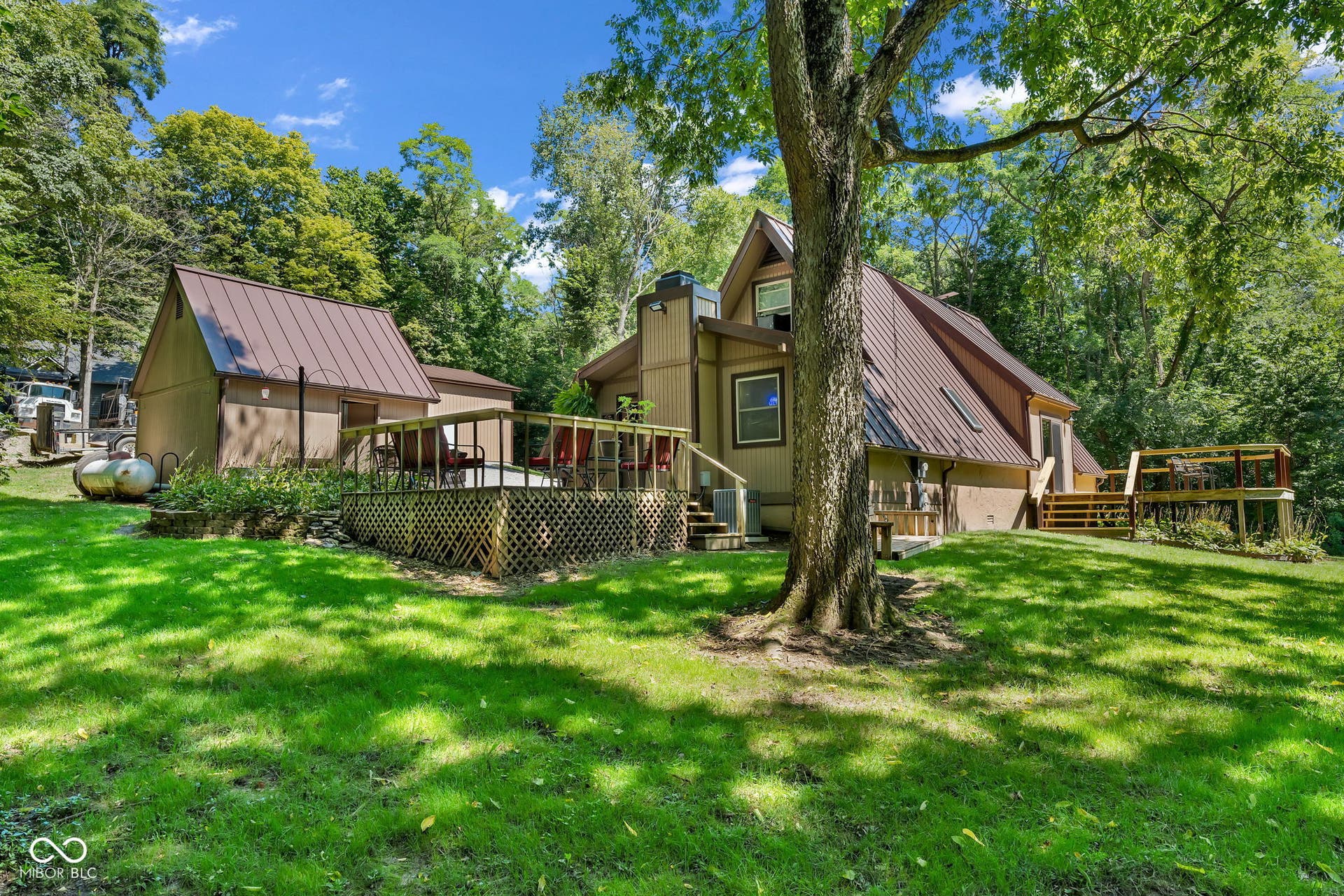 5432 W Whittier Drive, Knightstown, IN 46148 Expansive green lawn with mature trees, a multi-level wood deck, and a separate outbuilding with a metal roof