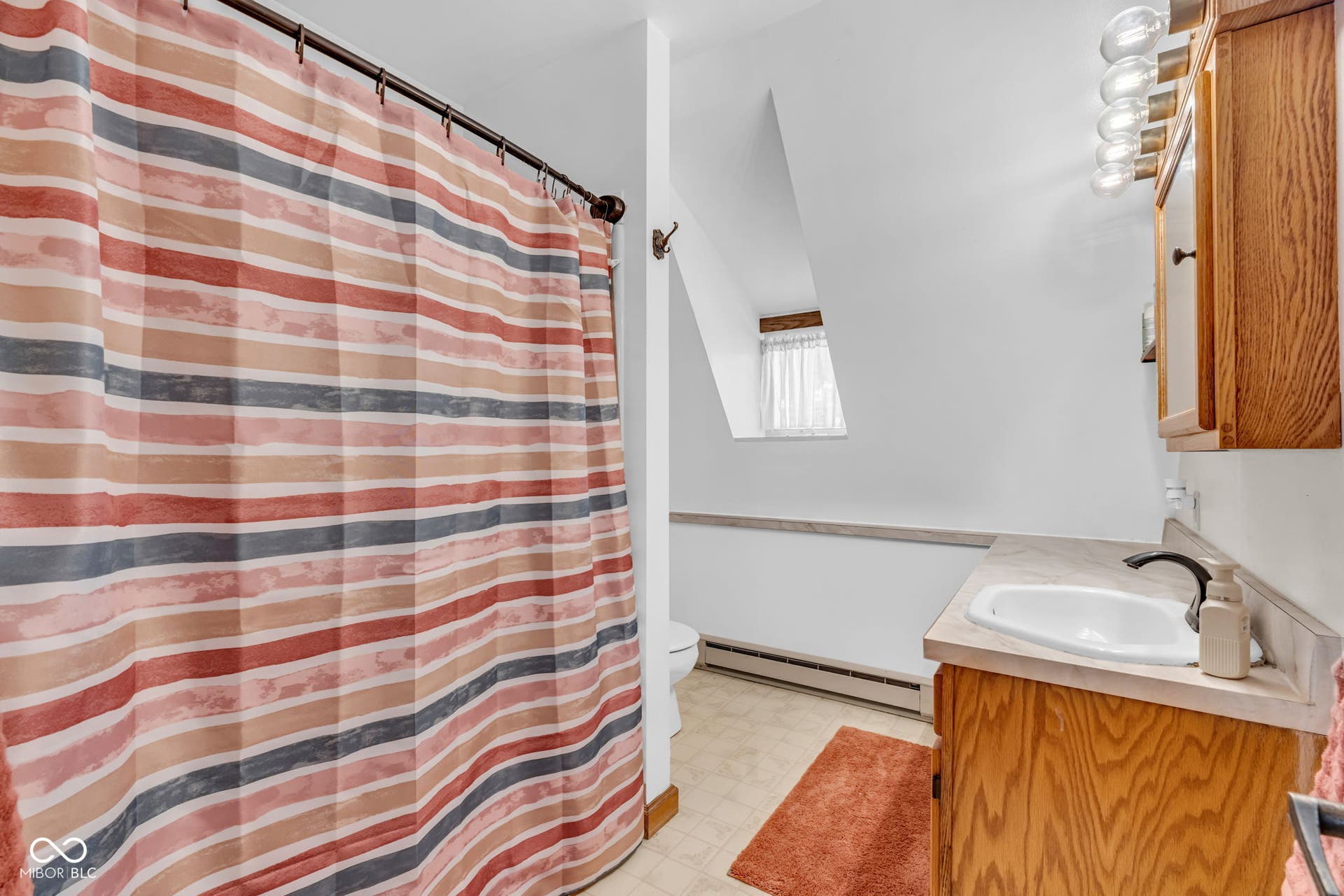 5432 W Whittier Drive, Knightstown, IN 46148 Wood-finish vanity with an integrated sink and matte black faucet, wall-mounted light fixture, and an angled ceiling with a window