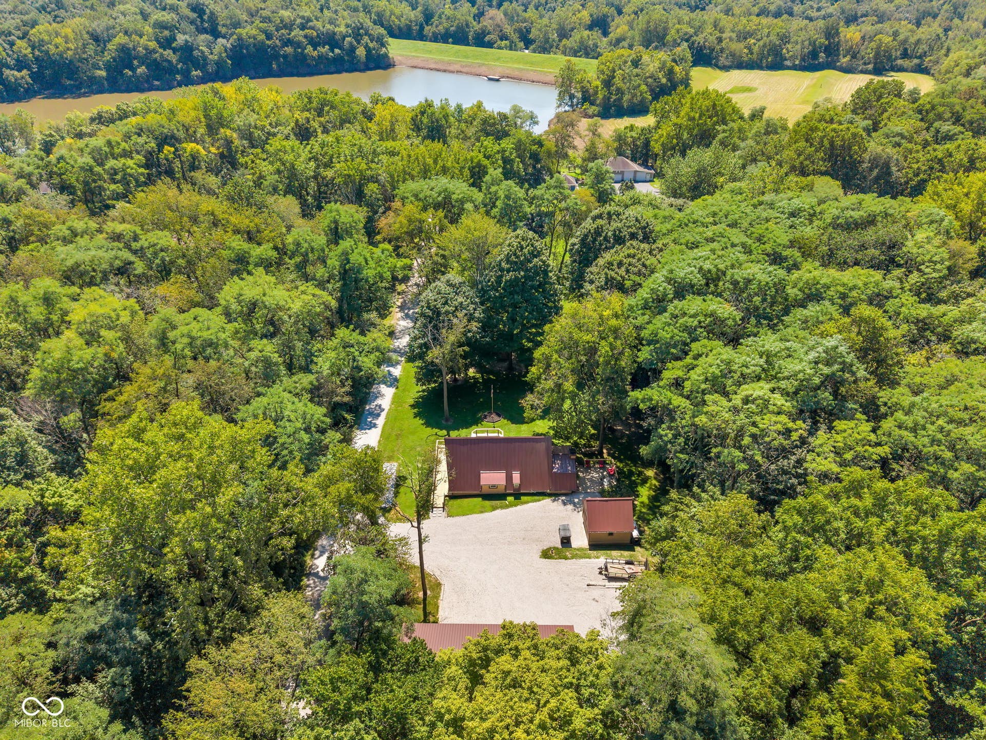 5432 W Whittier Drive, Knightstown, IN 46148 Wooded property featuring multiple structures, a gravel driveway, and a natural water body