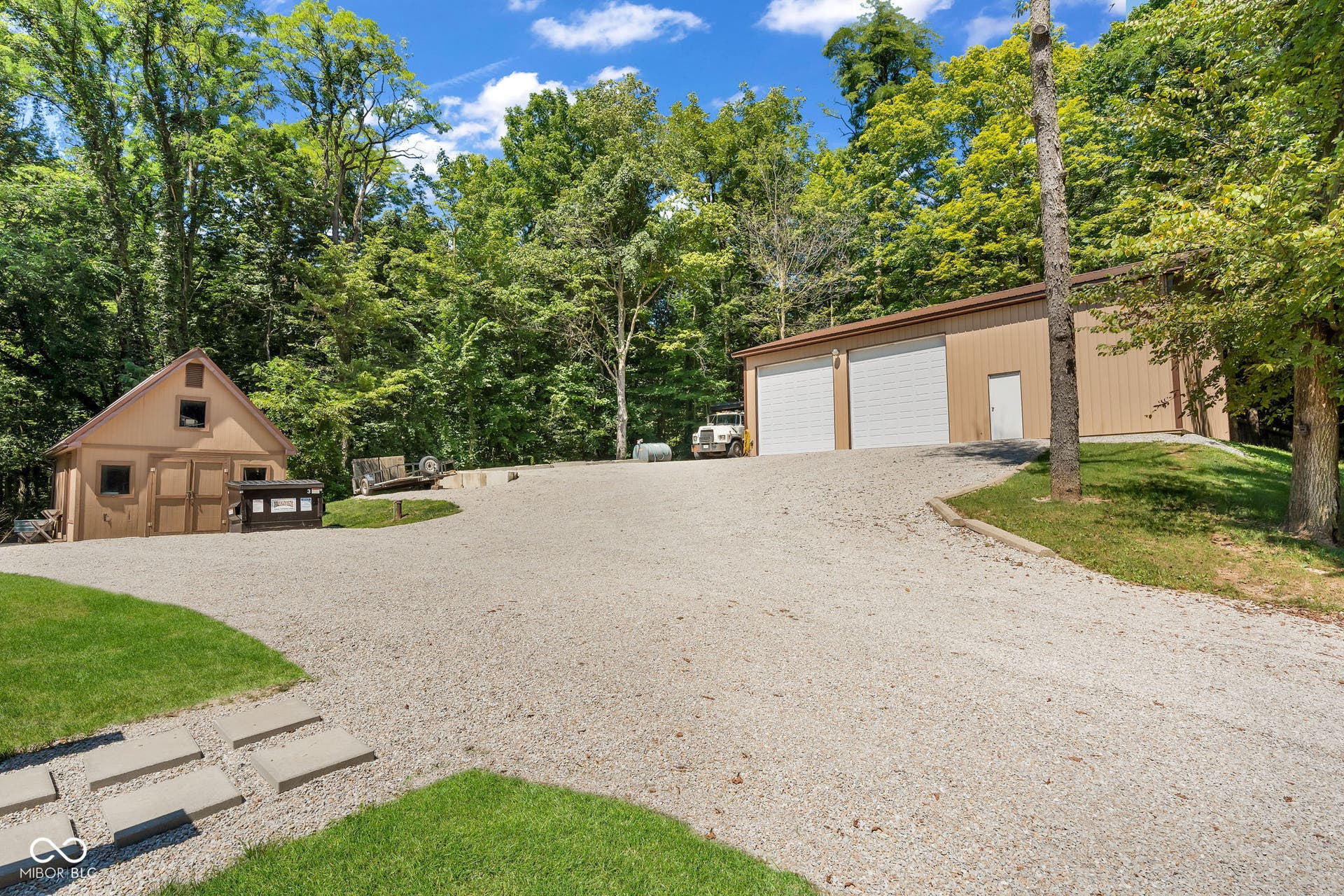 5432 W Whittier Drive, Knightstown, IN 46148 Expansive gravel driveway providing access to a multi-bay pole barn and a separate additional storage shed, all set amongst mature trees