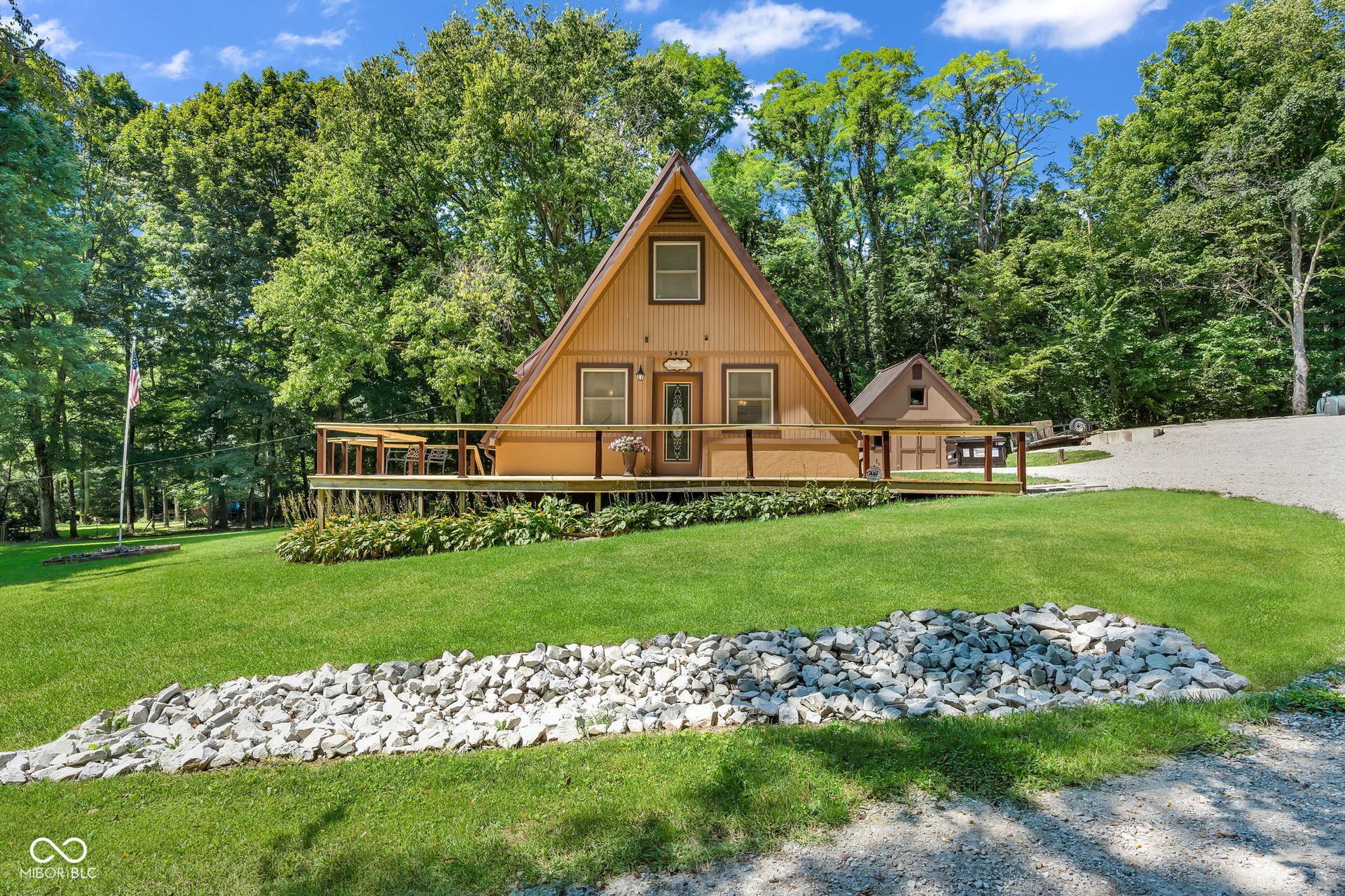 5432 W Whittier Drive, Knightstown, IN 46148 A-frame exterior with a spacious wooden deck, surrounded by mature trees and a verdant lawn