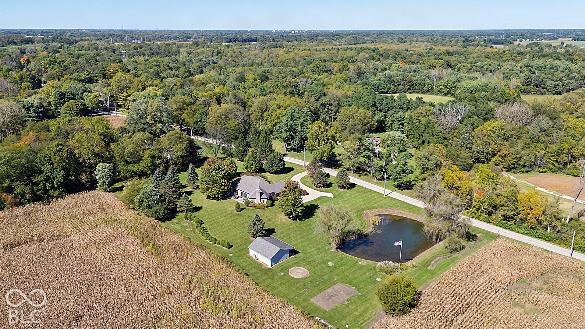 Expansive grounds featuring a pond, mature trees, manicured lawns, a detached outbuilding, and a curved driveway