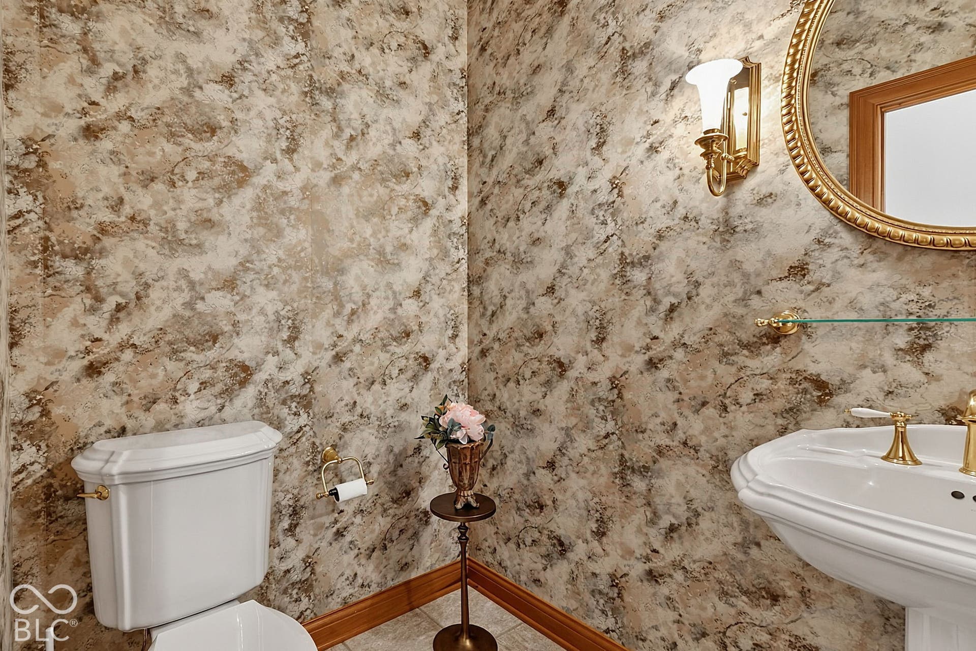 Pedestal sink with brass-finish faucet, ornate wall sconce, and round mirror with a decorative frame
