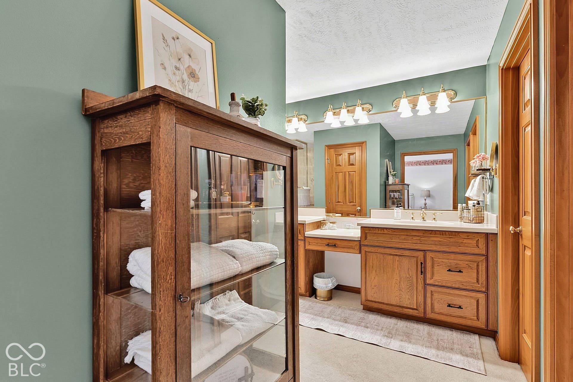 Built-in wood-finish cabinetry, dual vanity with undermount sinks, and a large wall-mounted mirror with integrated lighting
