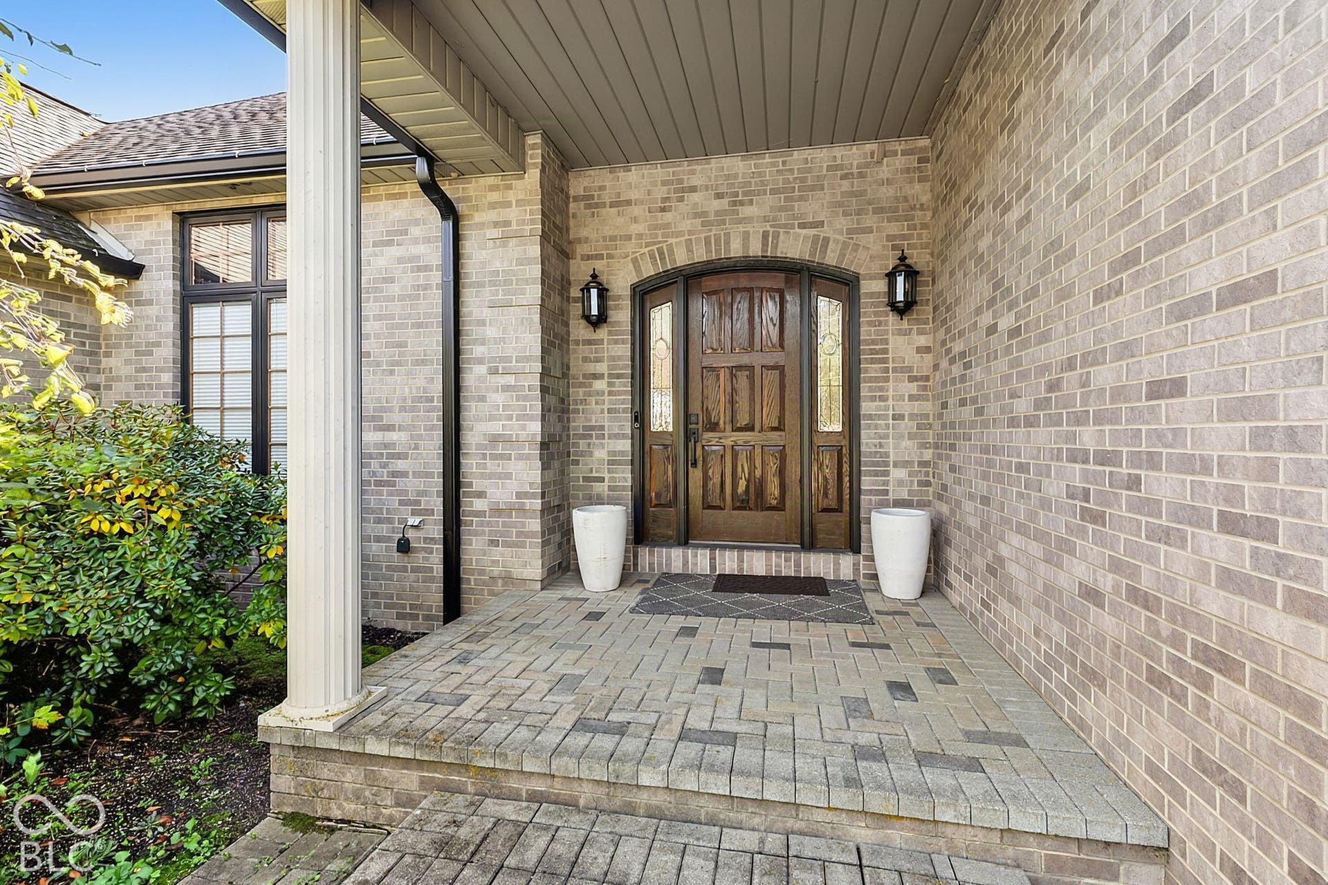 Brick exterior with an arched wooden entry door, flanked by two wall-mounted lanterns and decorative sidelights