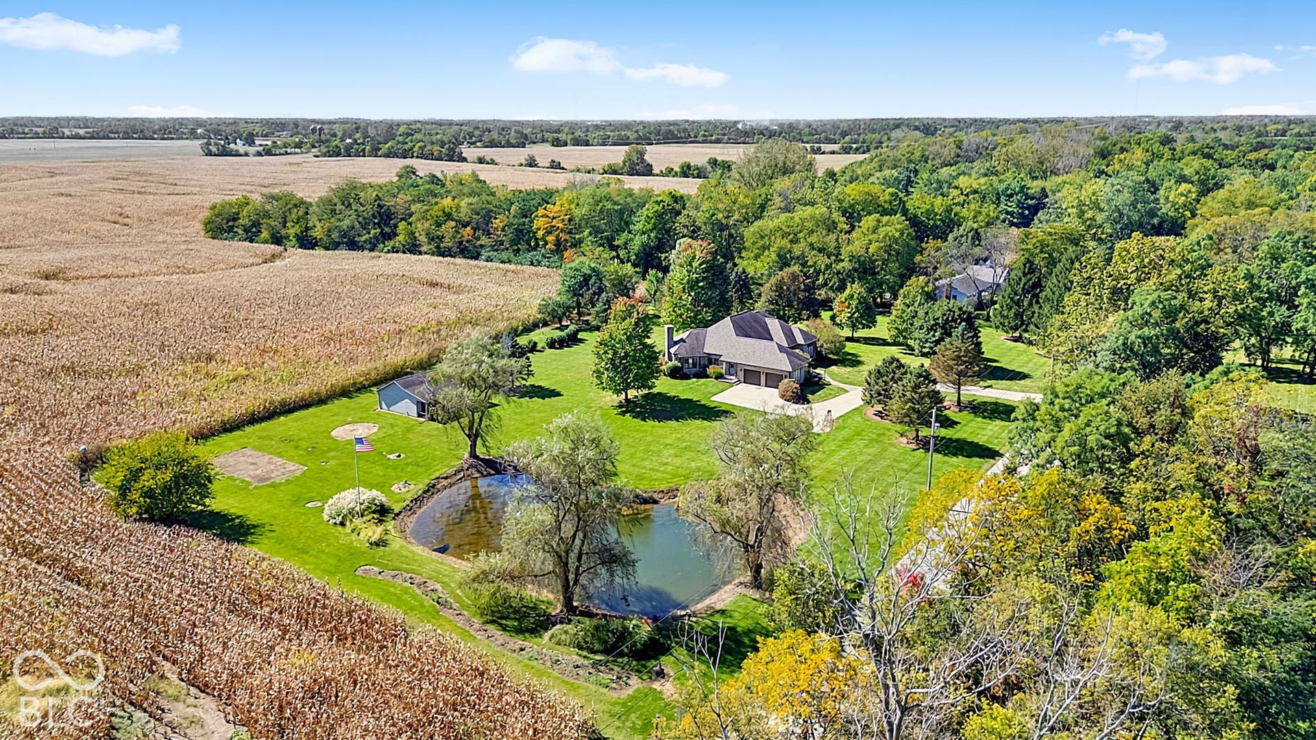 Expansive grounds featuring a private pond, lush green lawns, and mature trees, bordered by fields