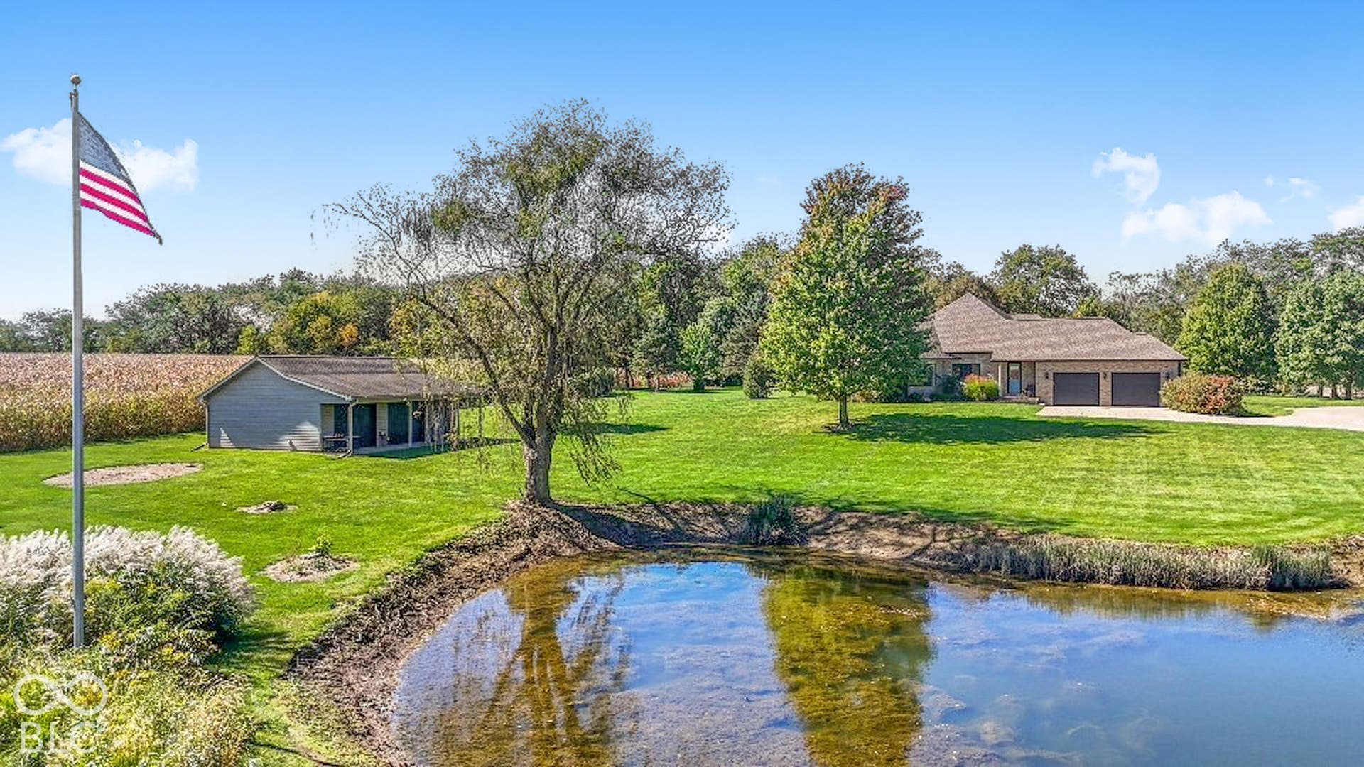 Expansive property featuring a tranquil pond, a detached auxiliary building, and a brick-finish residence with an attached two-car garage