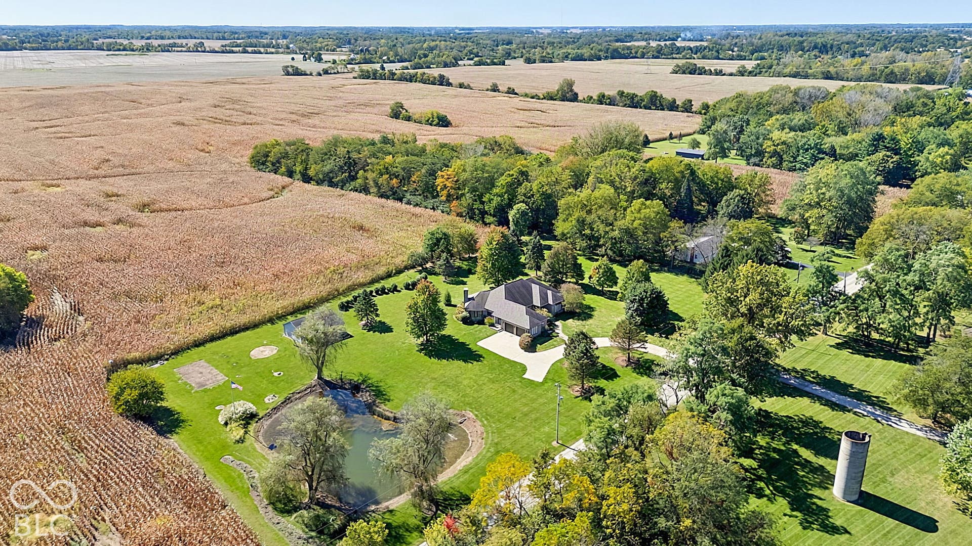 Expansive property featuring a large residence, circular driveway, mature trees, and a private pond